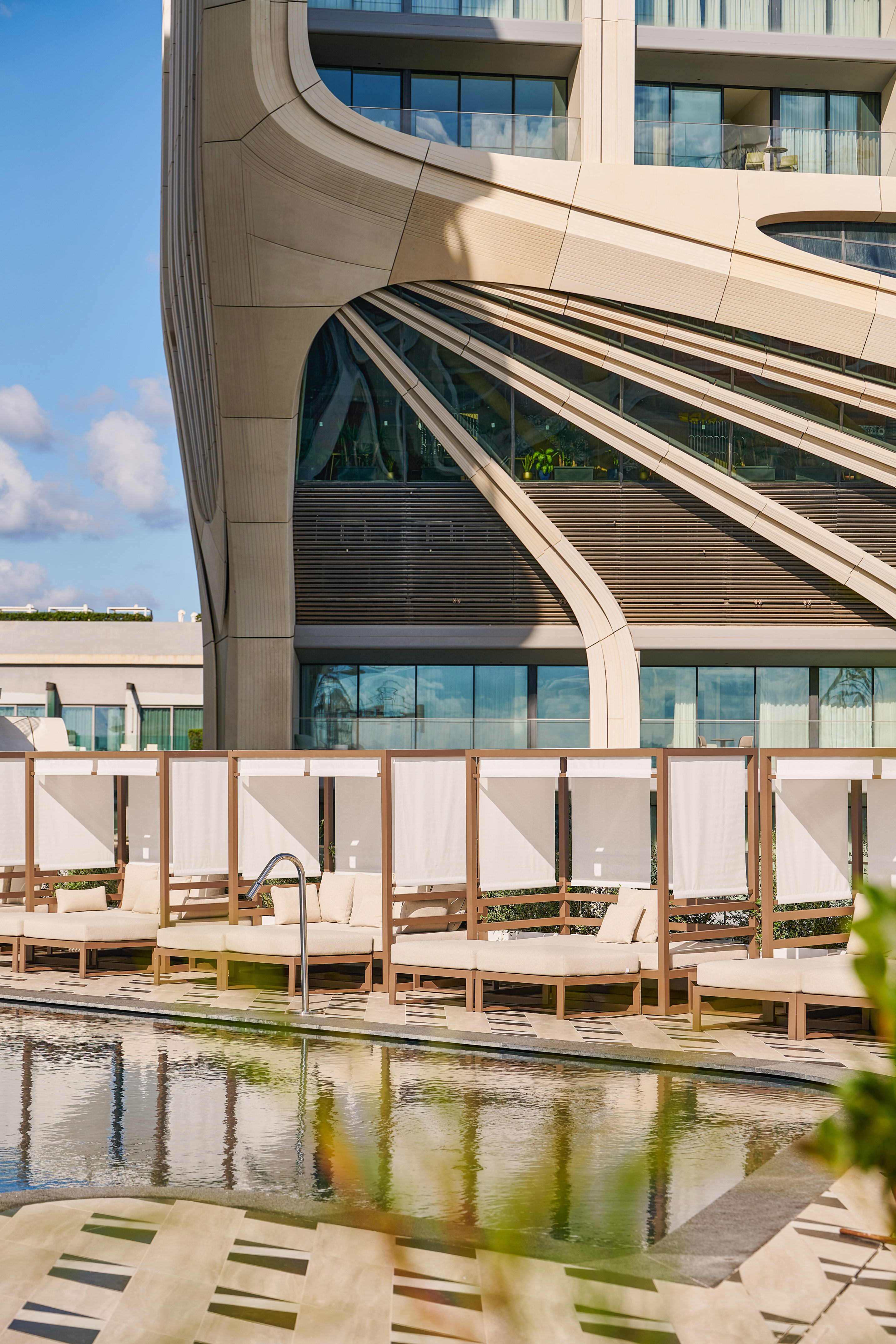 Luxury hotel with curved architecture, poolside cabanas, and reflecting pool.