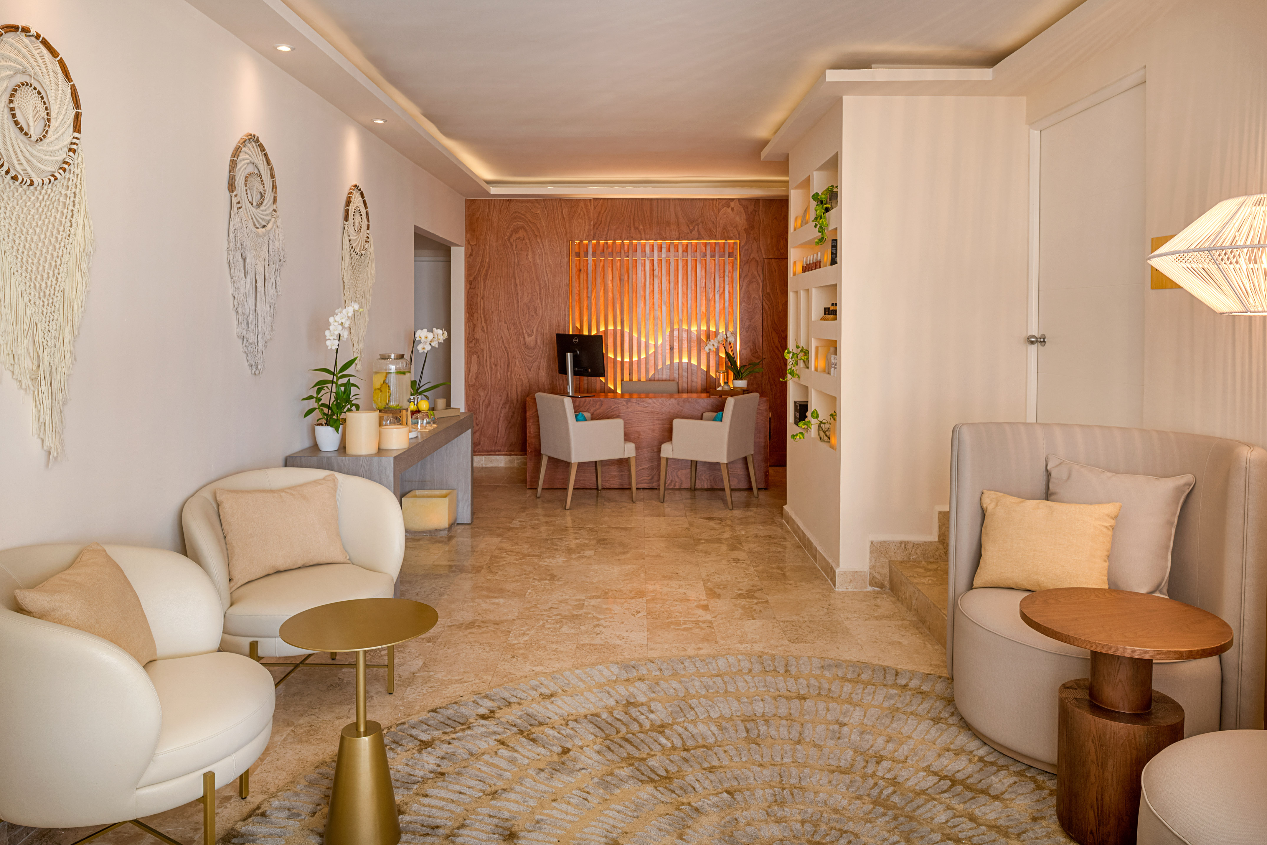Modern hotel lobby reception area with white armchairs, wooden desk, and macrame decor.