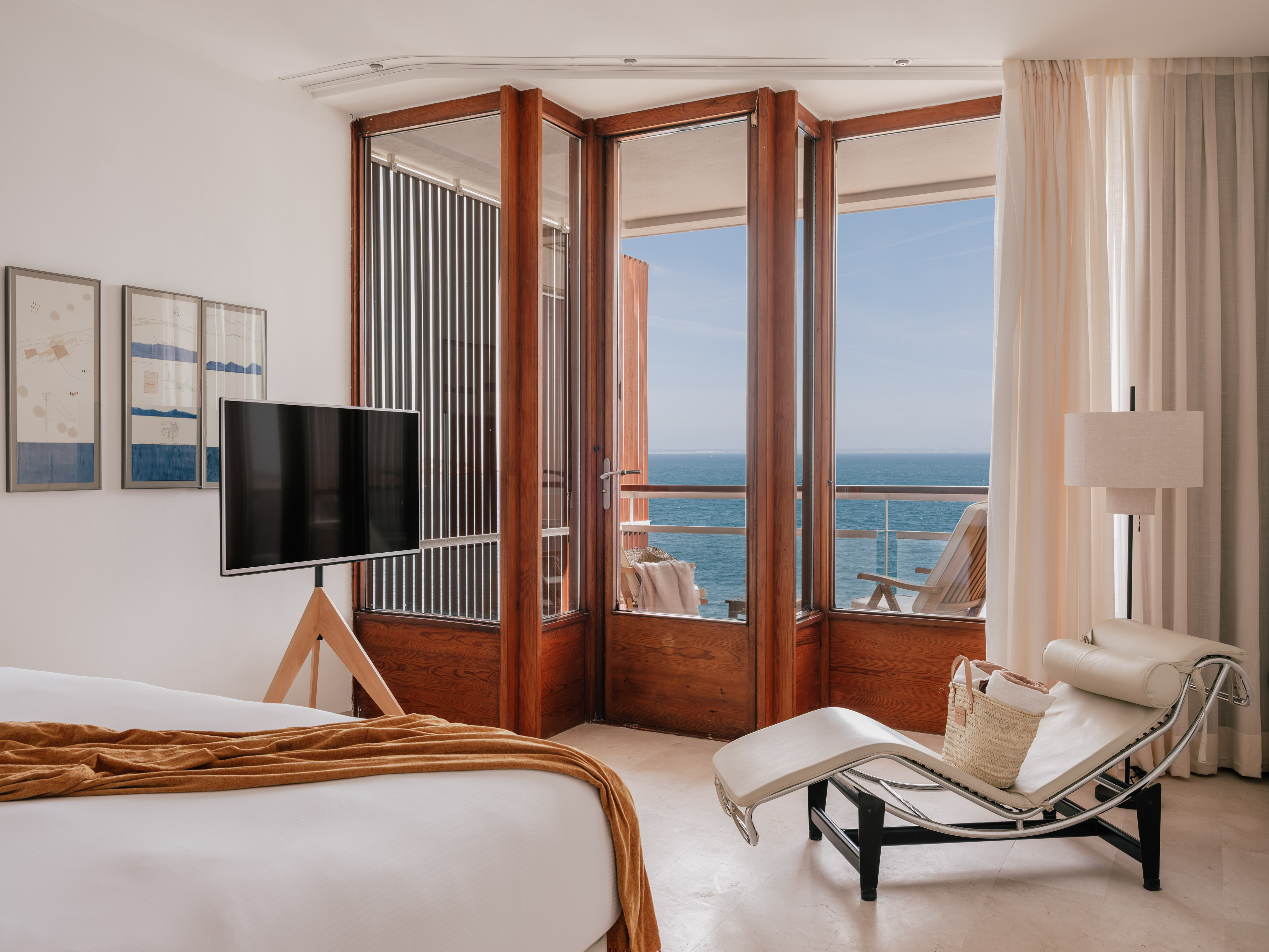 Modern hotel bedroom with sea view, private balcony, and lounge chair.