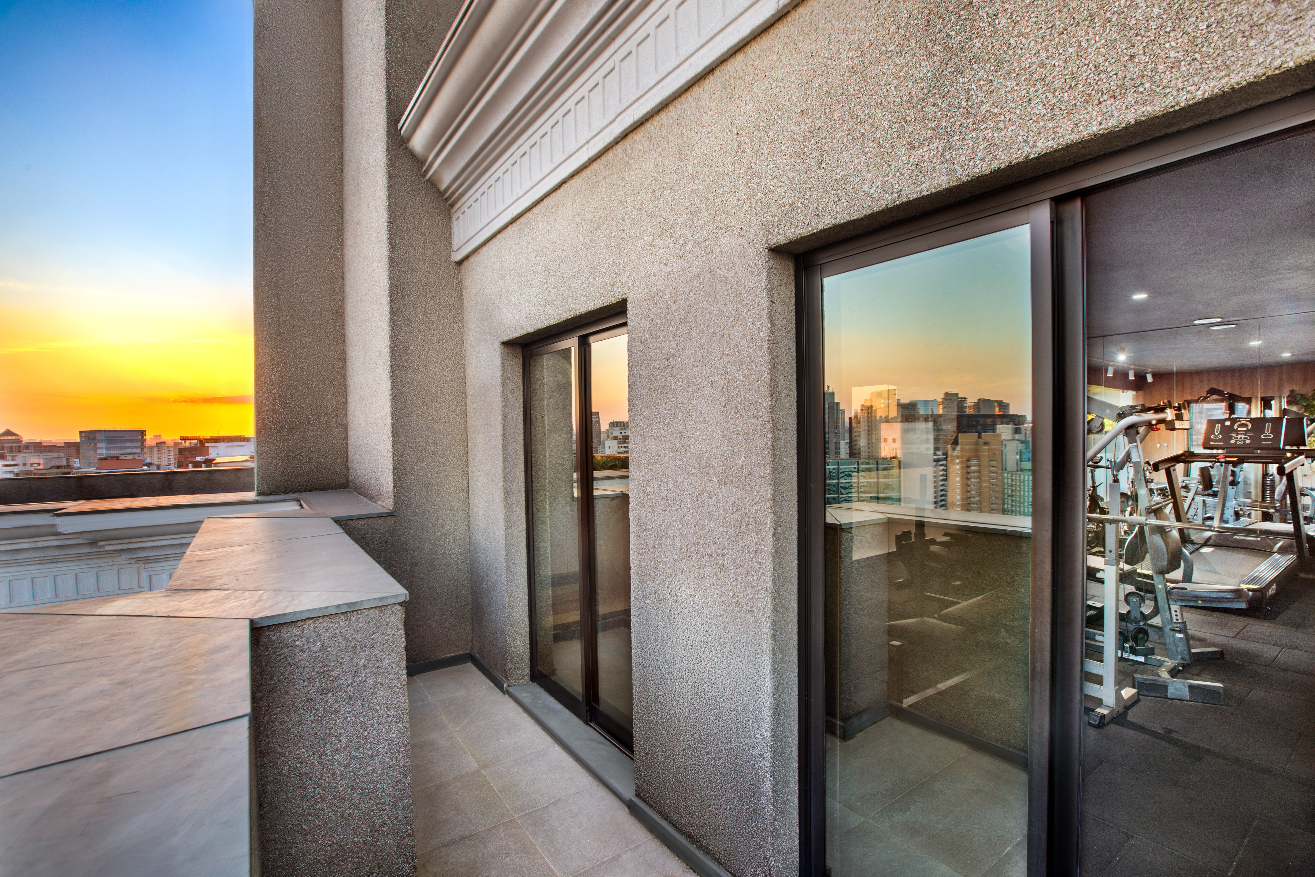Apartment balcony with sunset city view, reflecting a modern gym with fitness equipment.