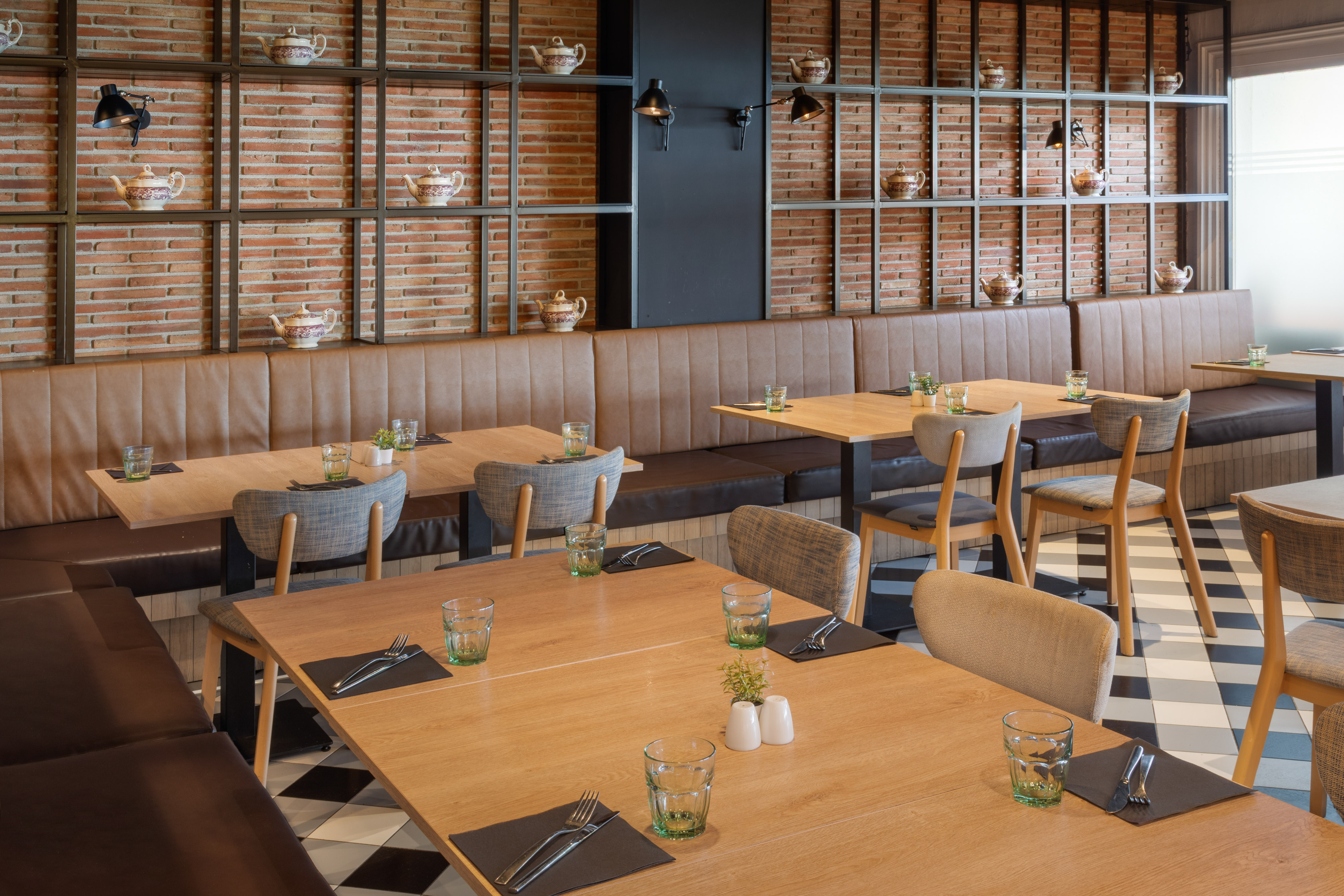 Restaurant with banquette seating, wooden tables, brick wall, and decorative teapots.