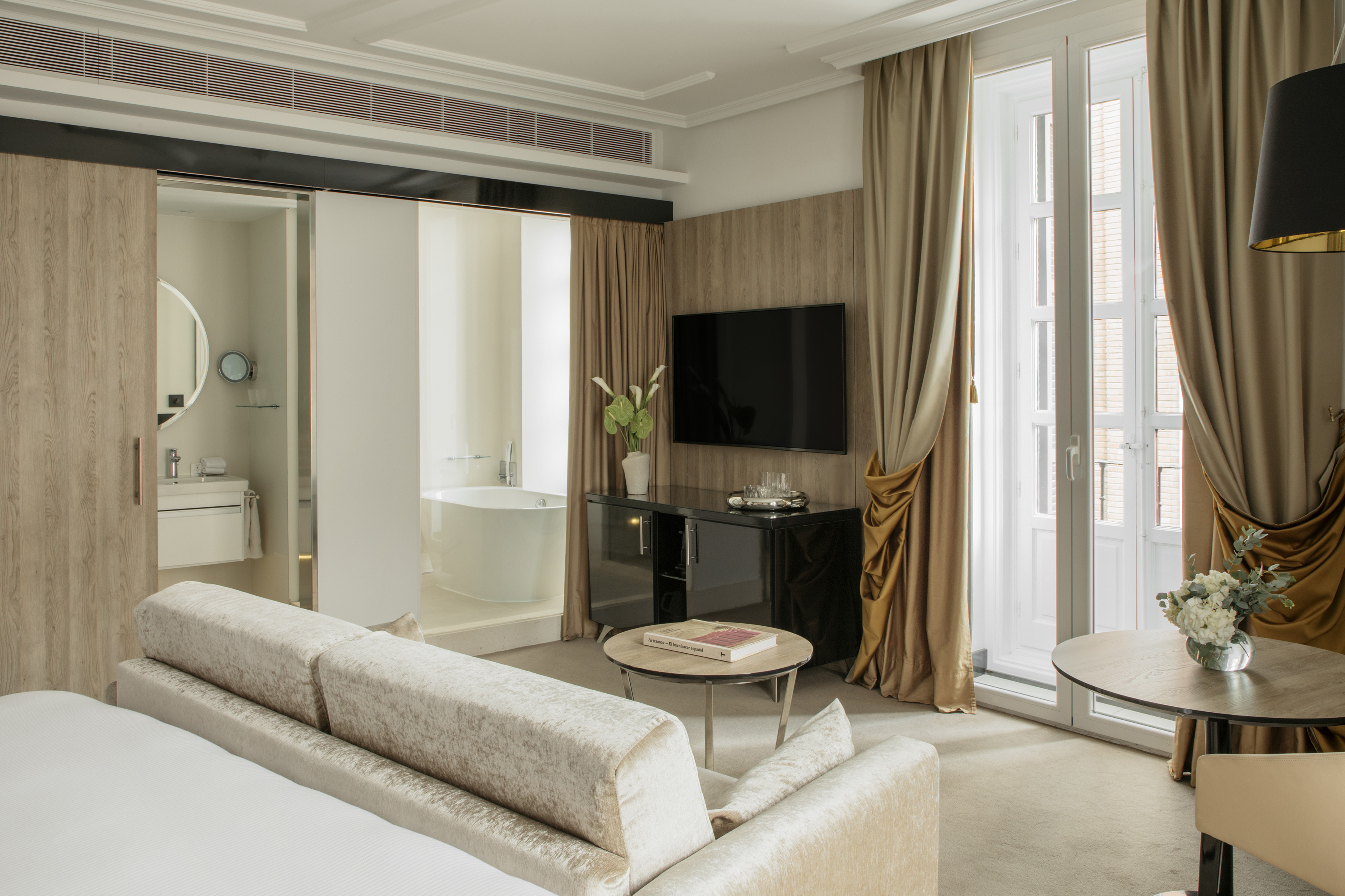 Luxury hotel suite with modern bedroom, open bathroom with tub, and balcony.