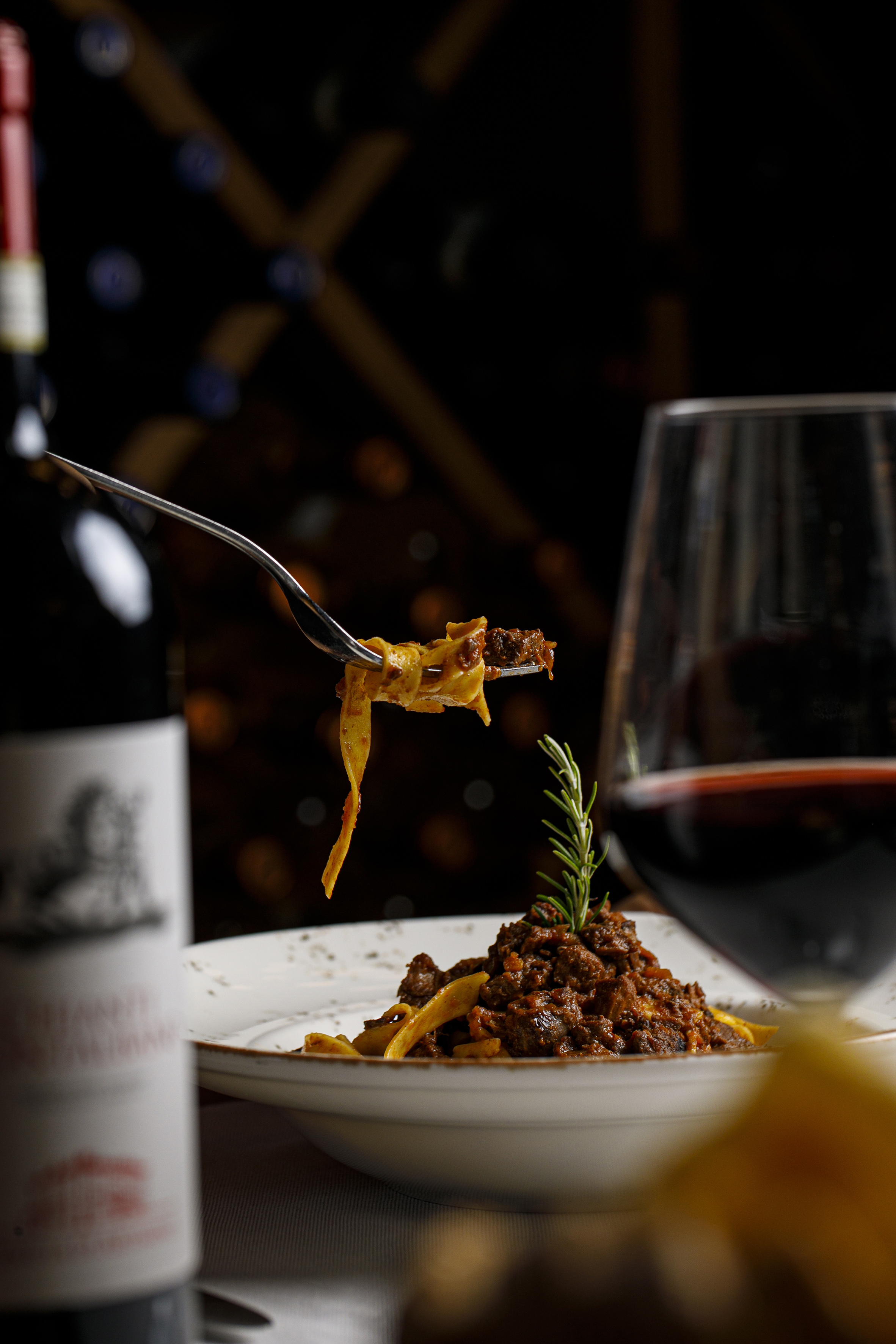 Italian pappardelle pasta with ragu on fork, red wine and rosemary.