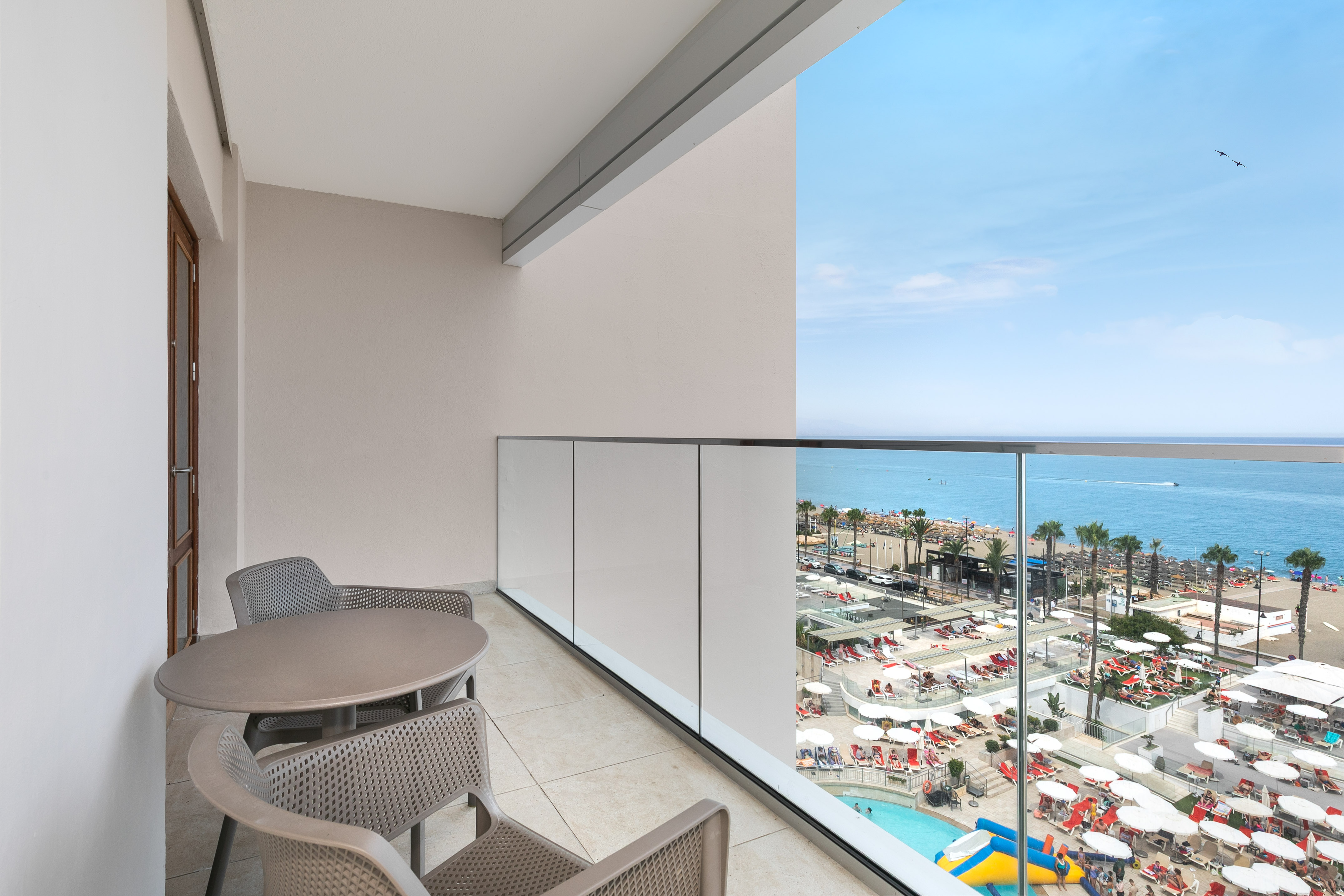 Balcony with sea view, sandy beach, resort pool, and palm trees.