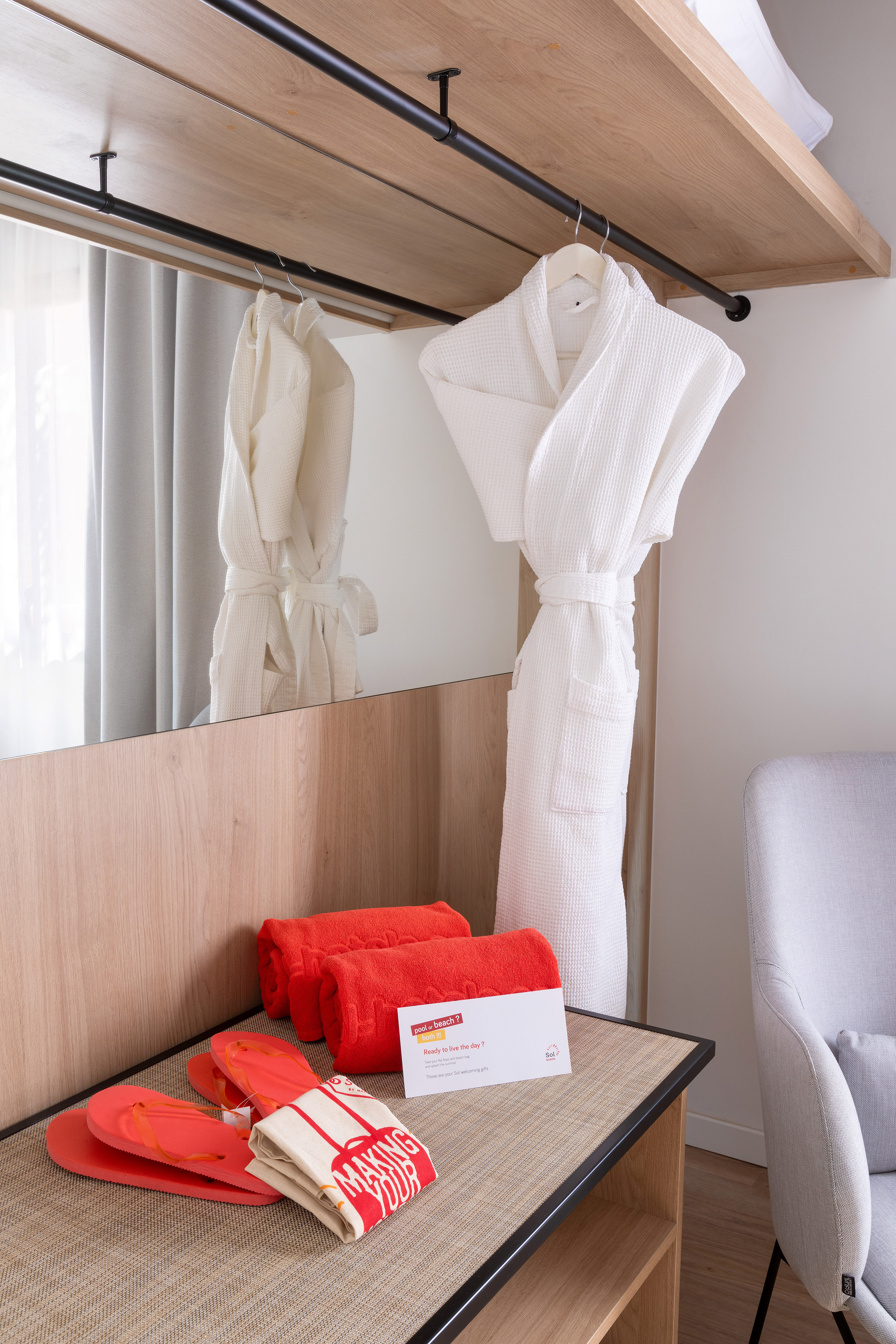 Hotel welcome amenities: white bathrobe, red towels, flip-flops, and beach bag.