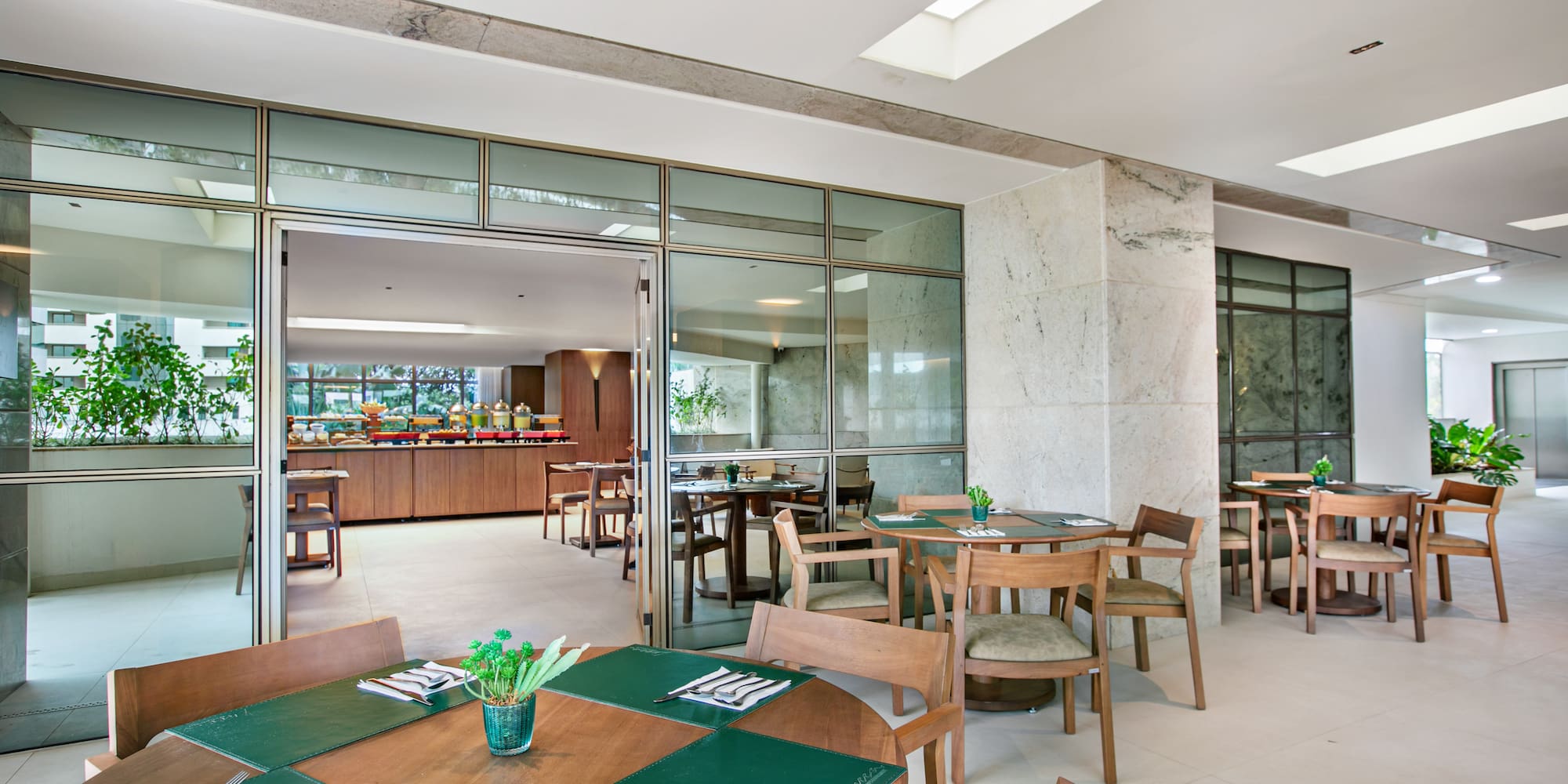 Hotel restaurant with modern wood tables, green placemats, and breakfast buffet.