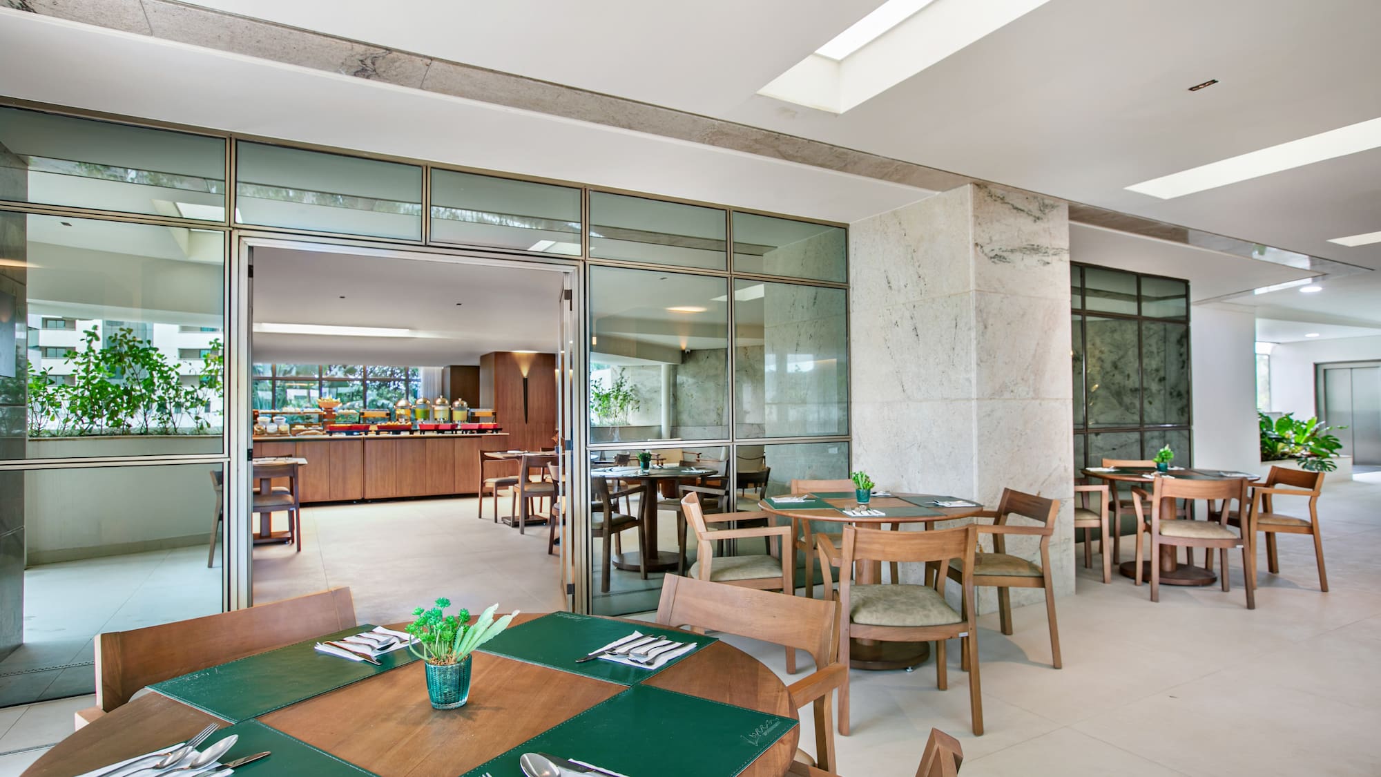 Hotel restaurant with modern wood tables, green placemats, and breakfast buffet.
