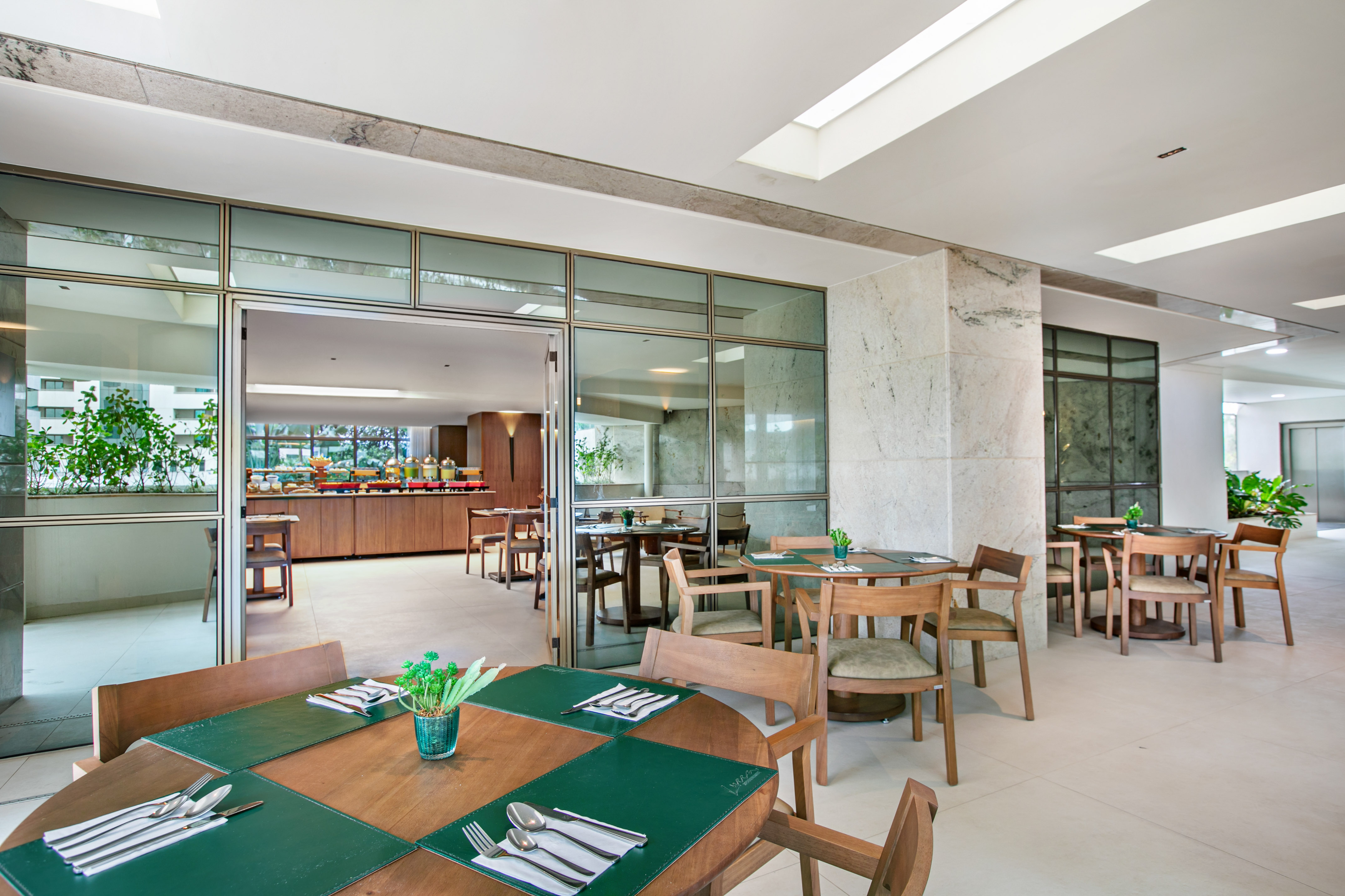 Hotel restaurant with modern wood tables, green placemats, and breakfast buffet.
