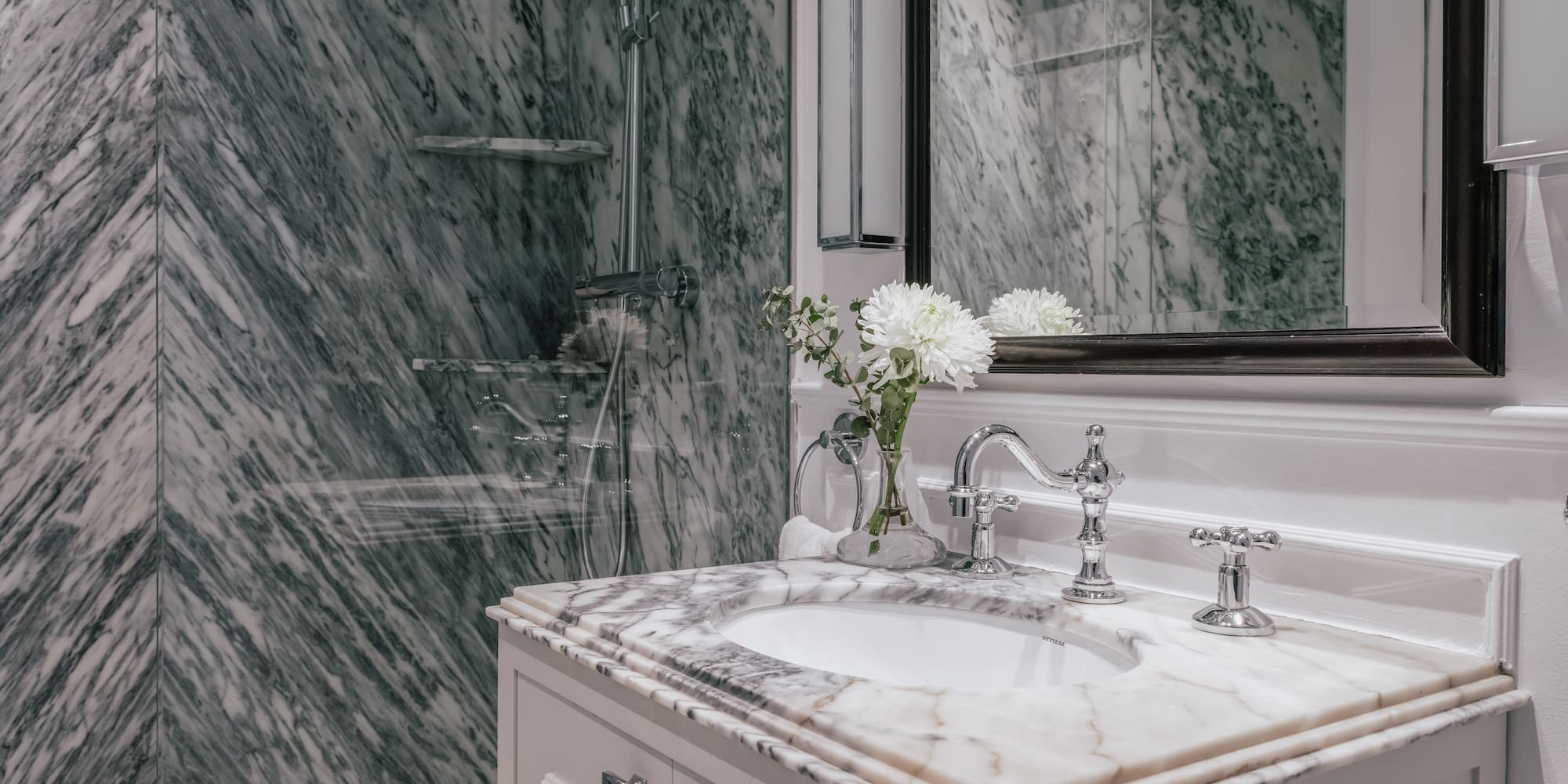 Elegant marble bathroom with white vanity, chrome fixtures, and glass shower.