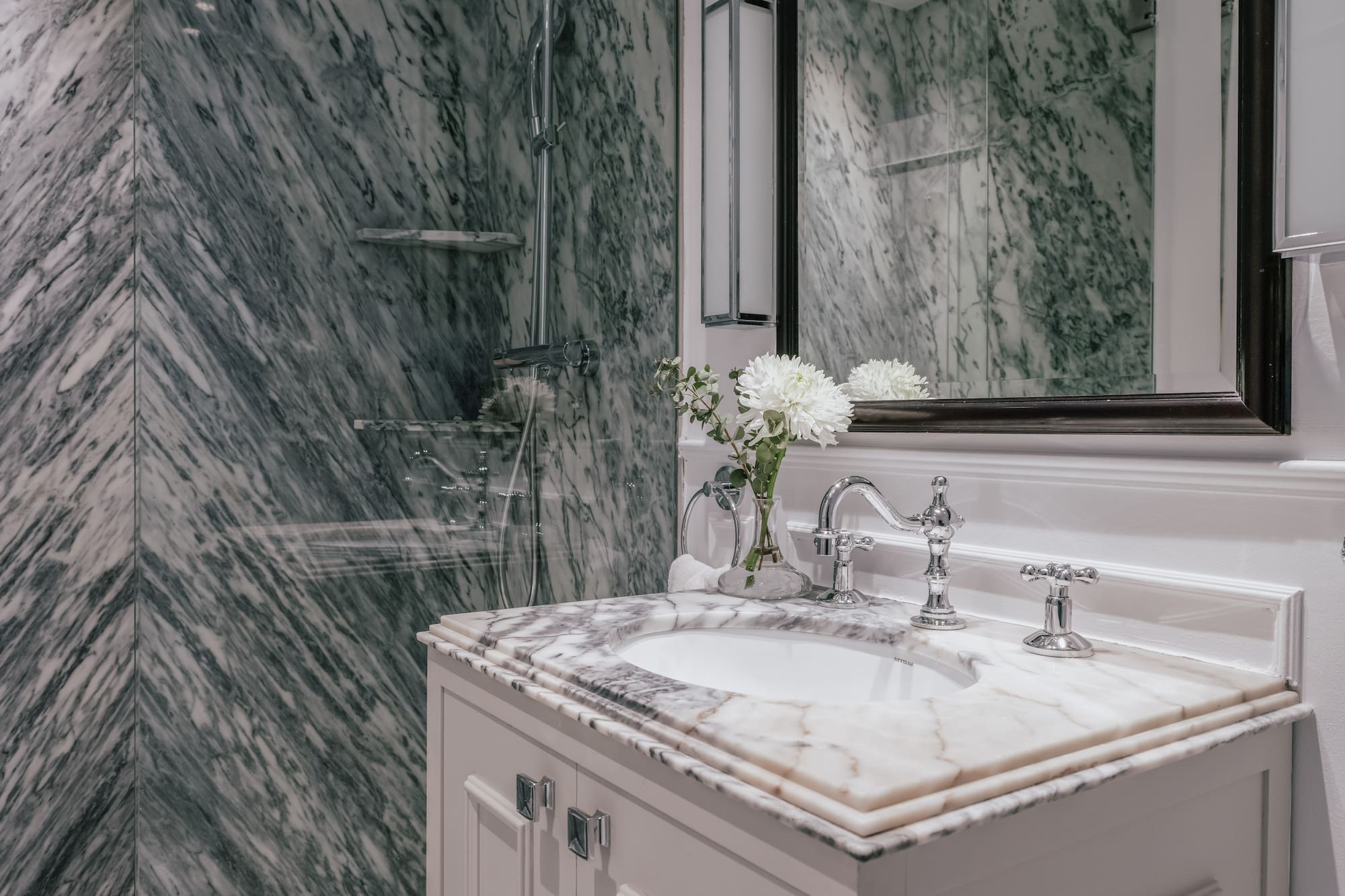 Elegant marble bathroom with white vanity, chrome fixtures, and glass shower.