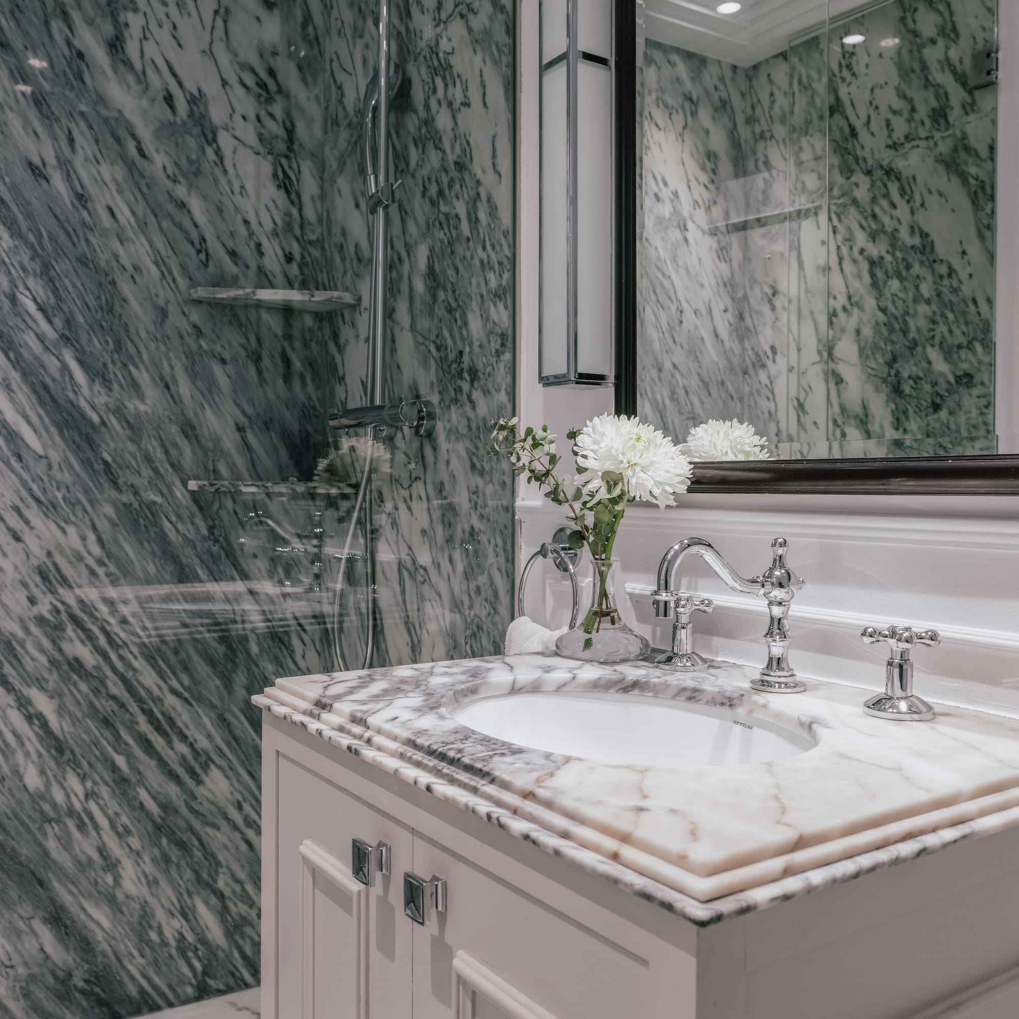 Elegant marble bathroom with white vanity, chrome fixtures, and glass shower.
