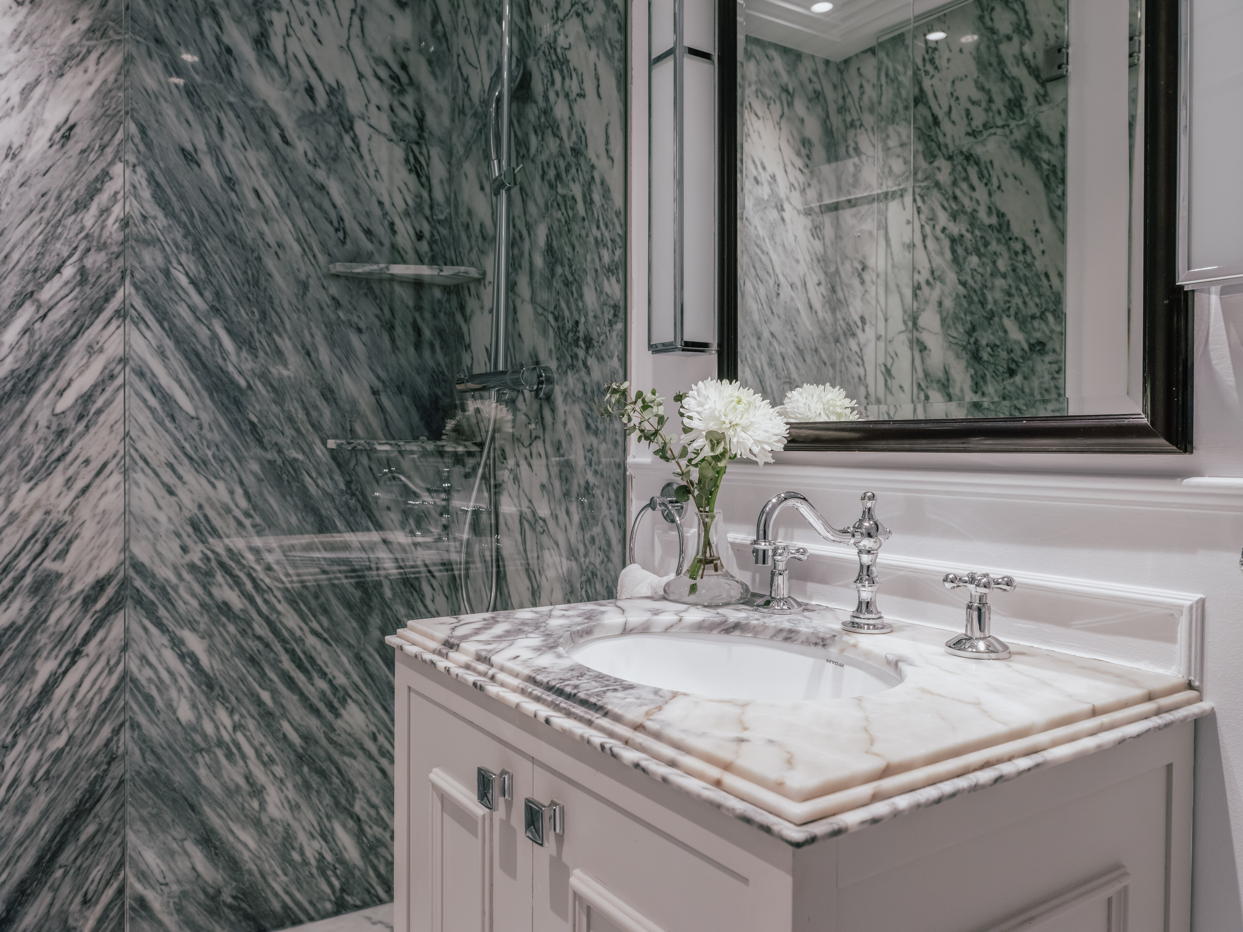 Elegant marble bathroom with white vanity, chrome fixtures, and glass shower.