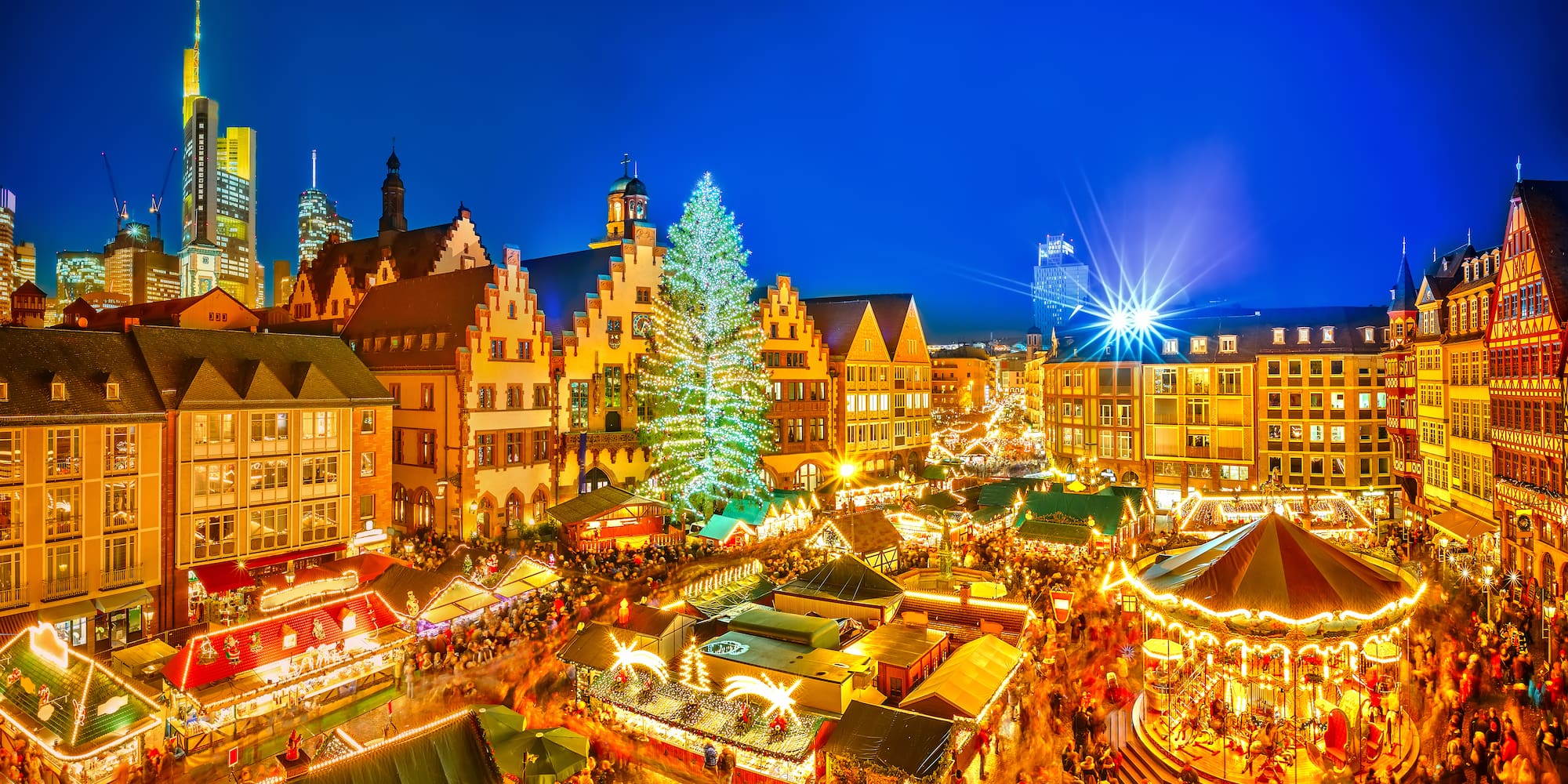 Frankfurt Christmas market at night with bright lights, festive tree, and stalls.