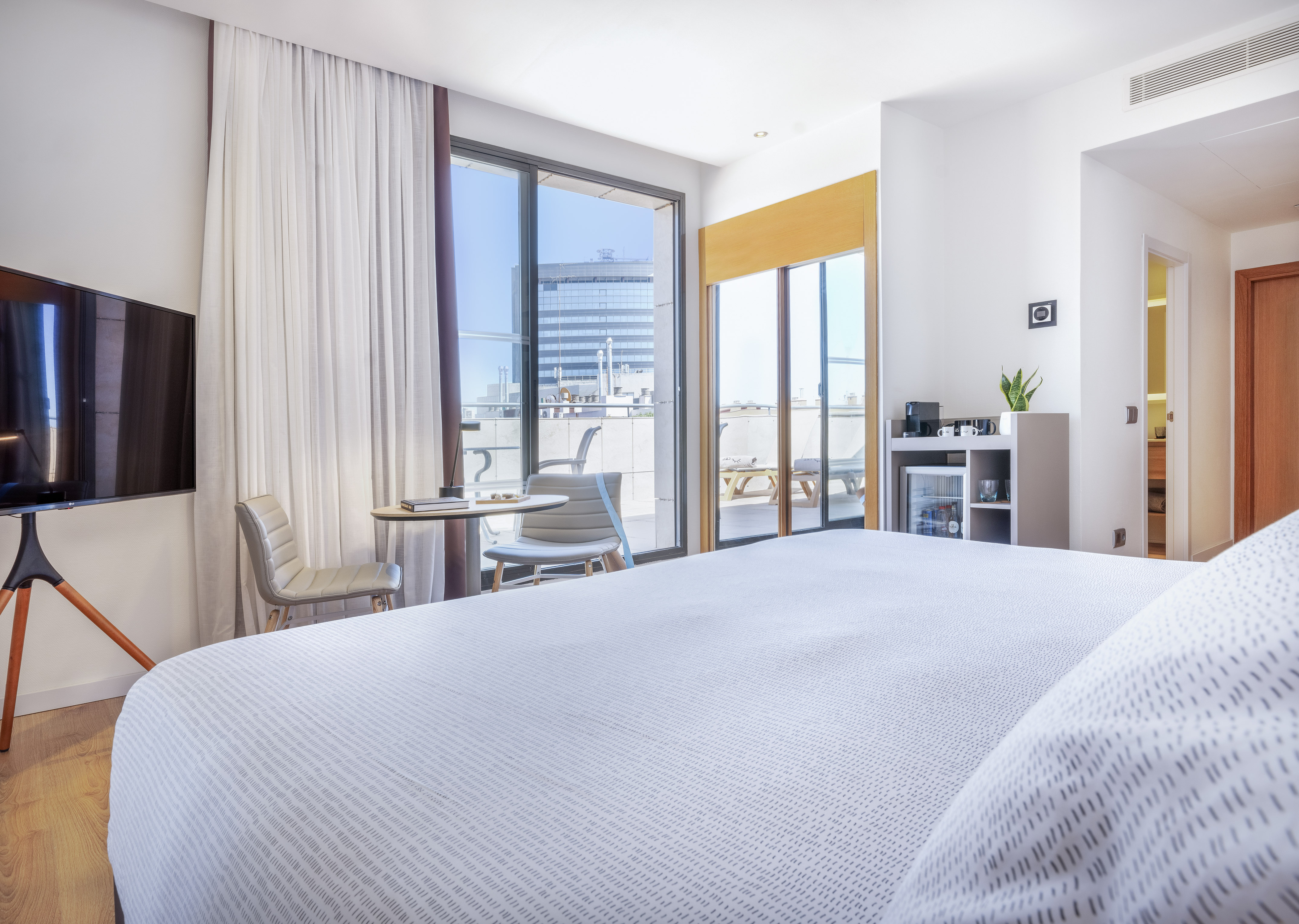 Modern hotel room with bed, private balcony, TV, and mini-bar amenities.