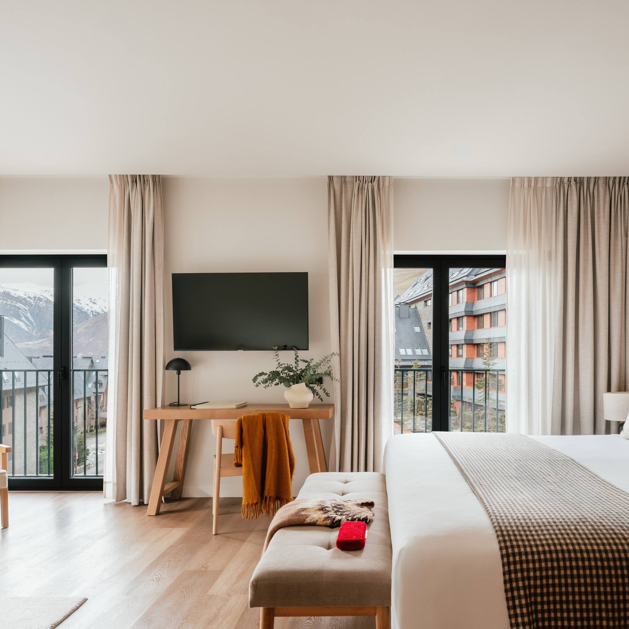 Modern hotel room with balcony, snowy mountain view, large bed, and workspace.