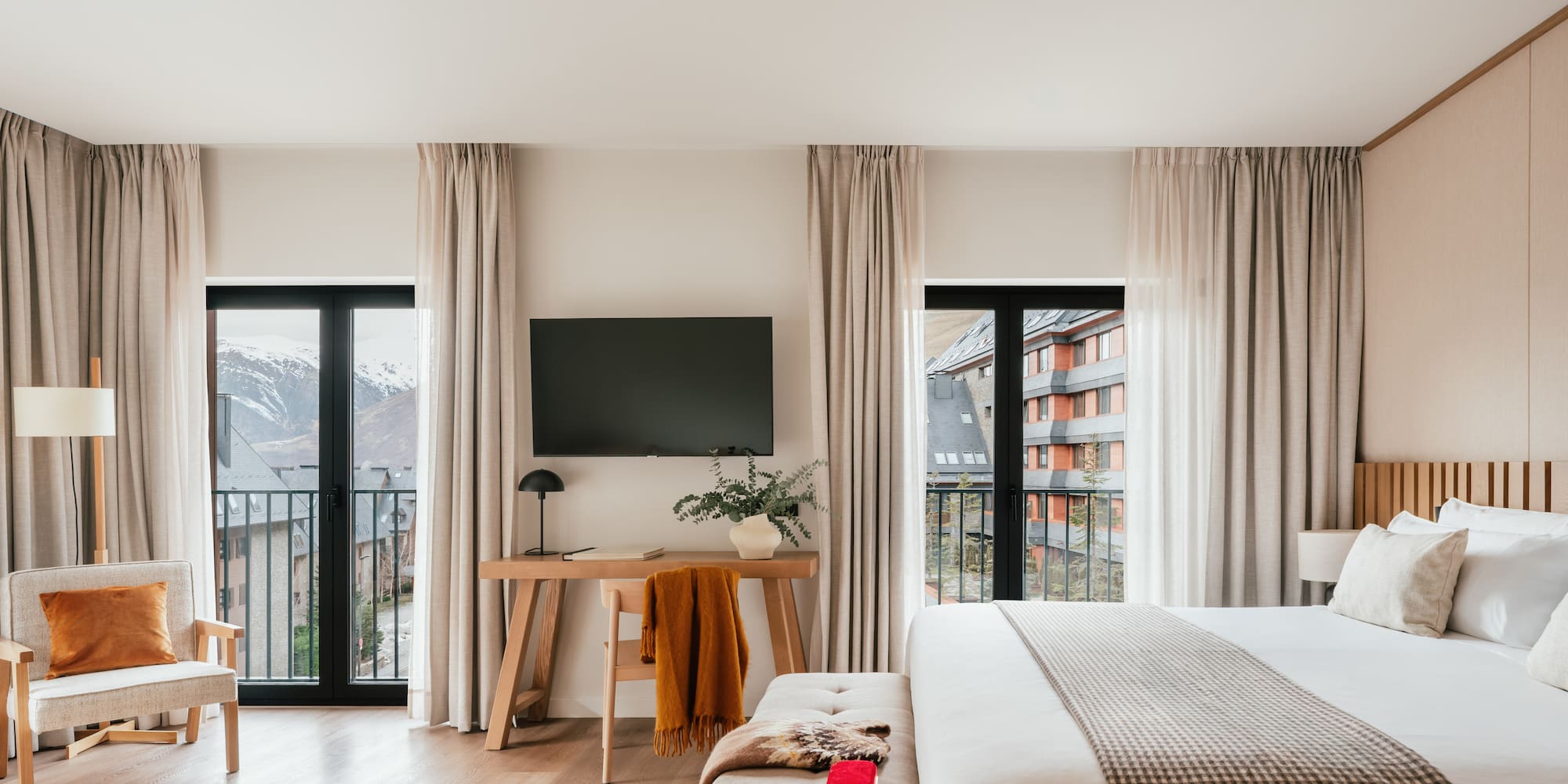 Modern hotel room with balcony, snowy mountain view, large bed, and workspace.