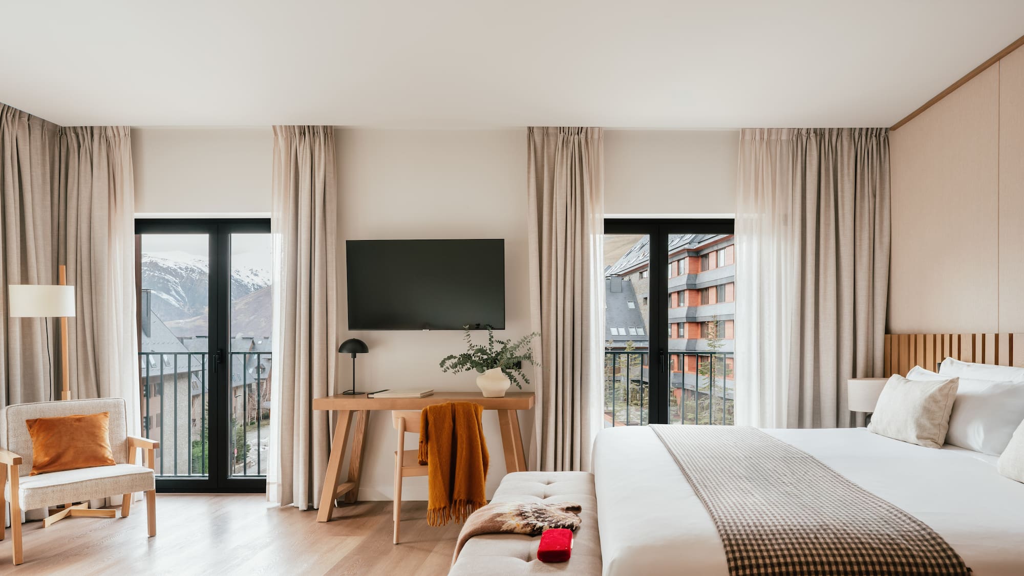 Modern hotel room with balcony, snowy mountain view, large bed, and workspace.