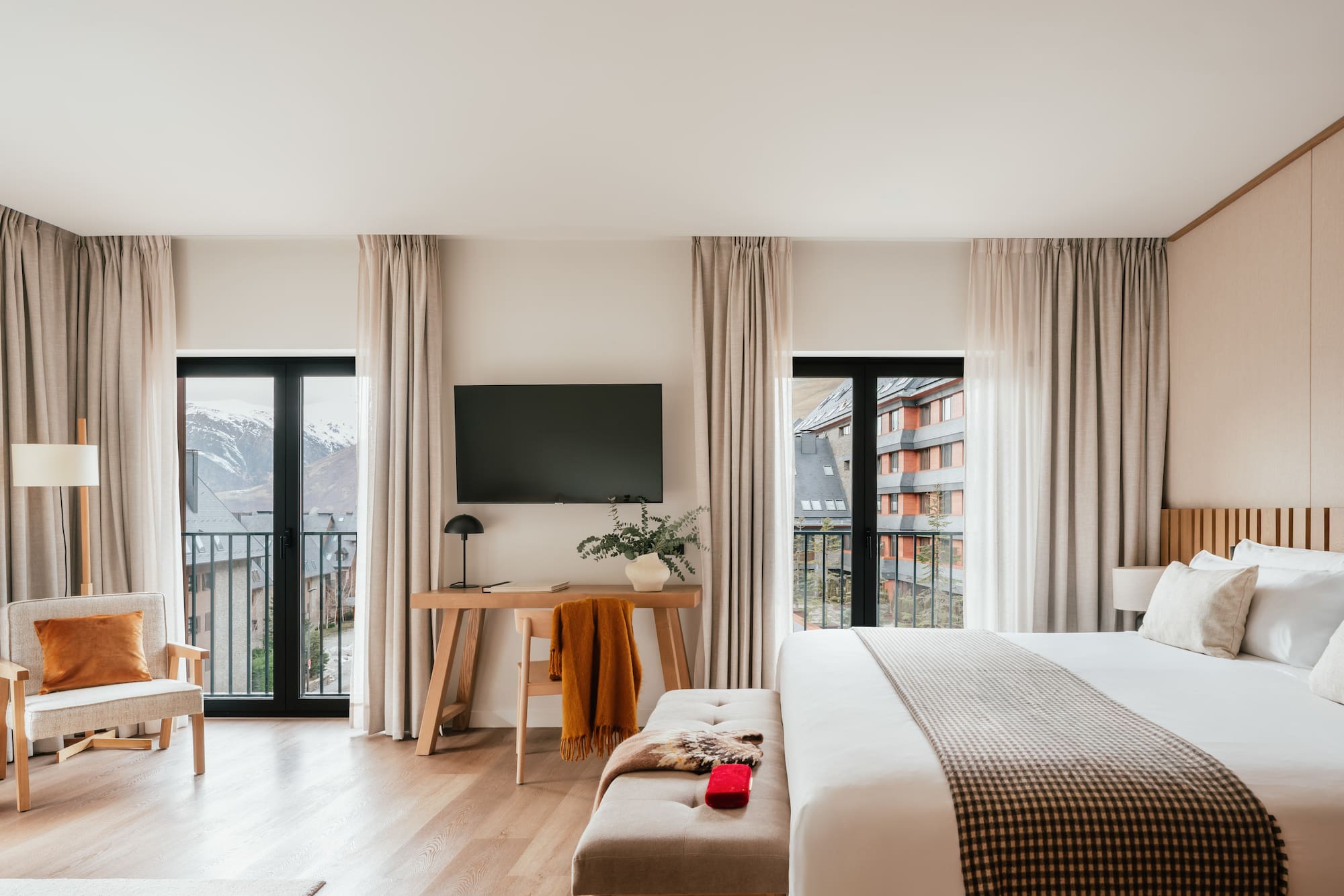 Modern hotel room with balcony, snowy mountain view, large bed, and workspace.