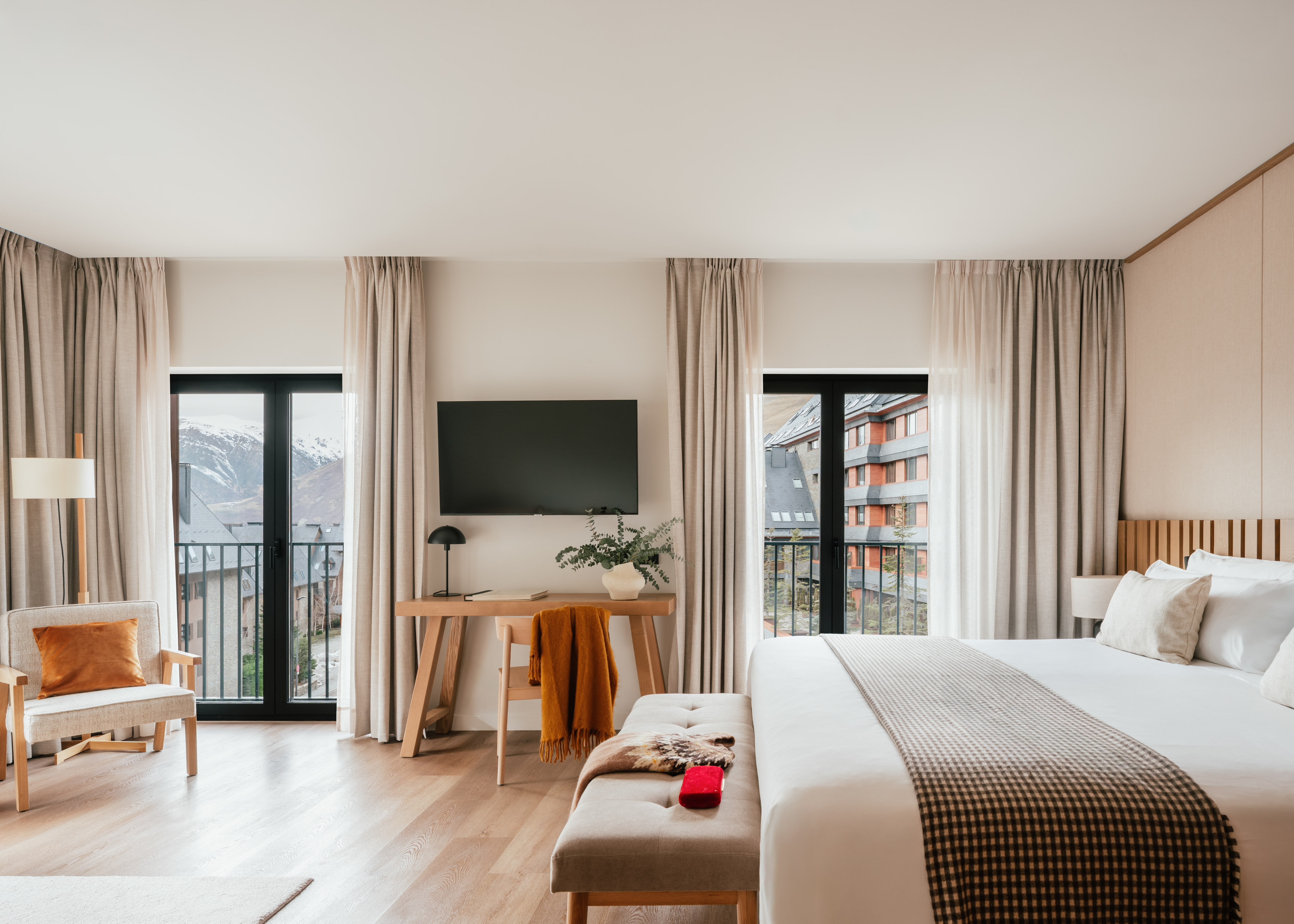 Modern hotel room with balcony, snowy mountain view, large bed, and workspace.
