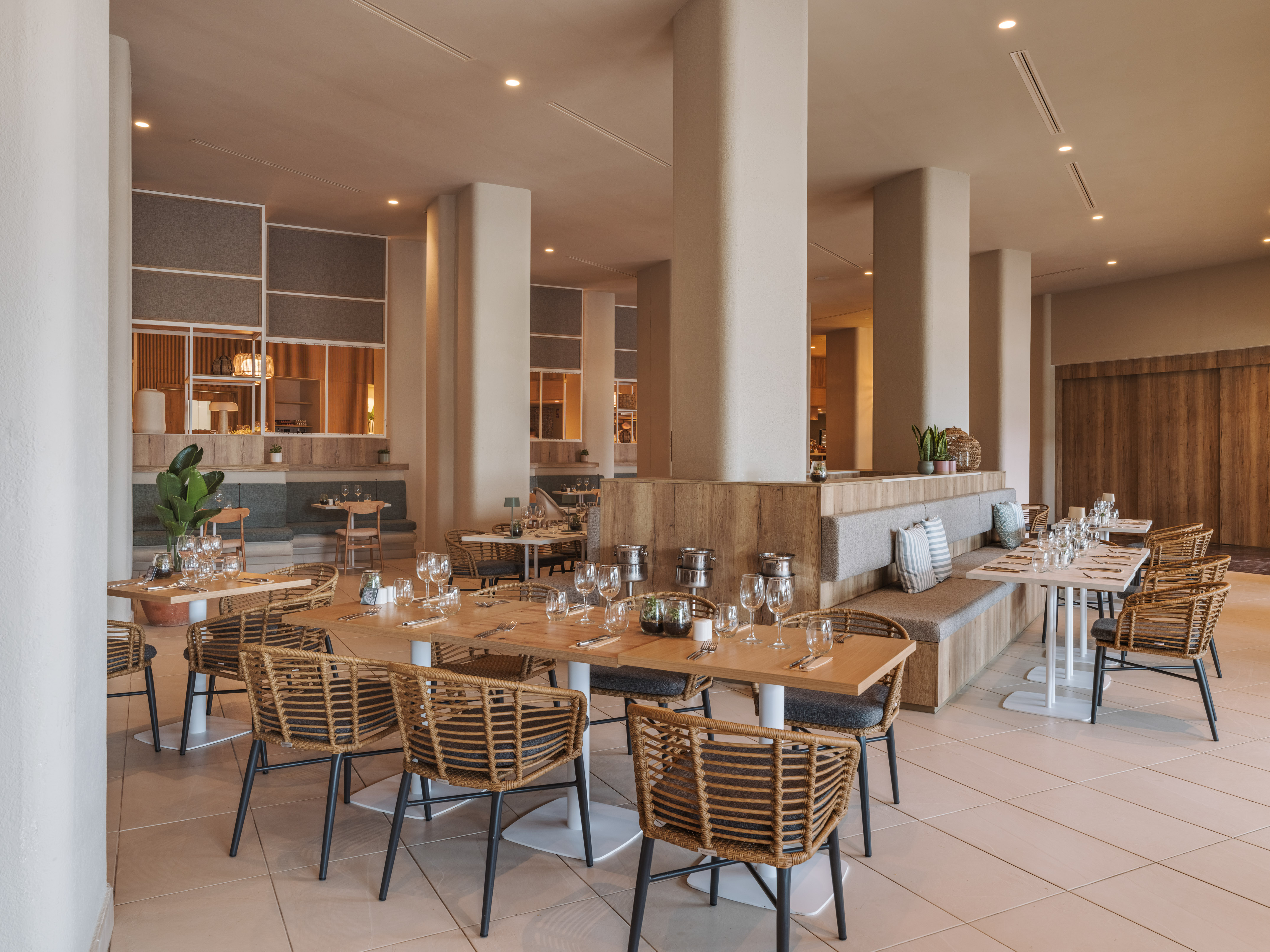 Contemporary restaurant interior with light wood tables, wicker chairs, and booth seating.