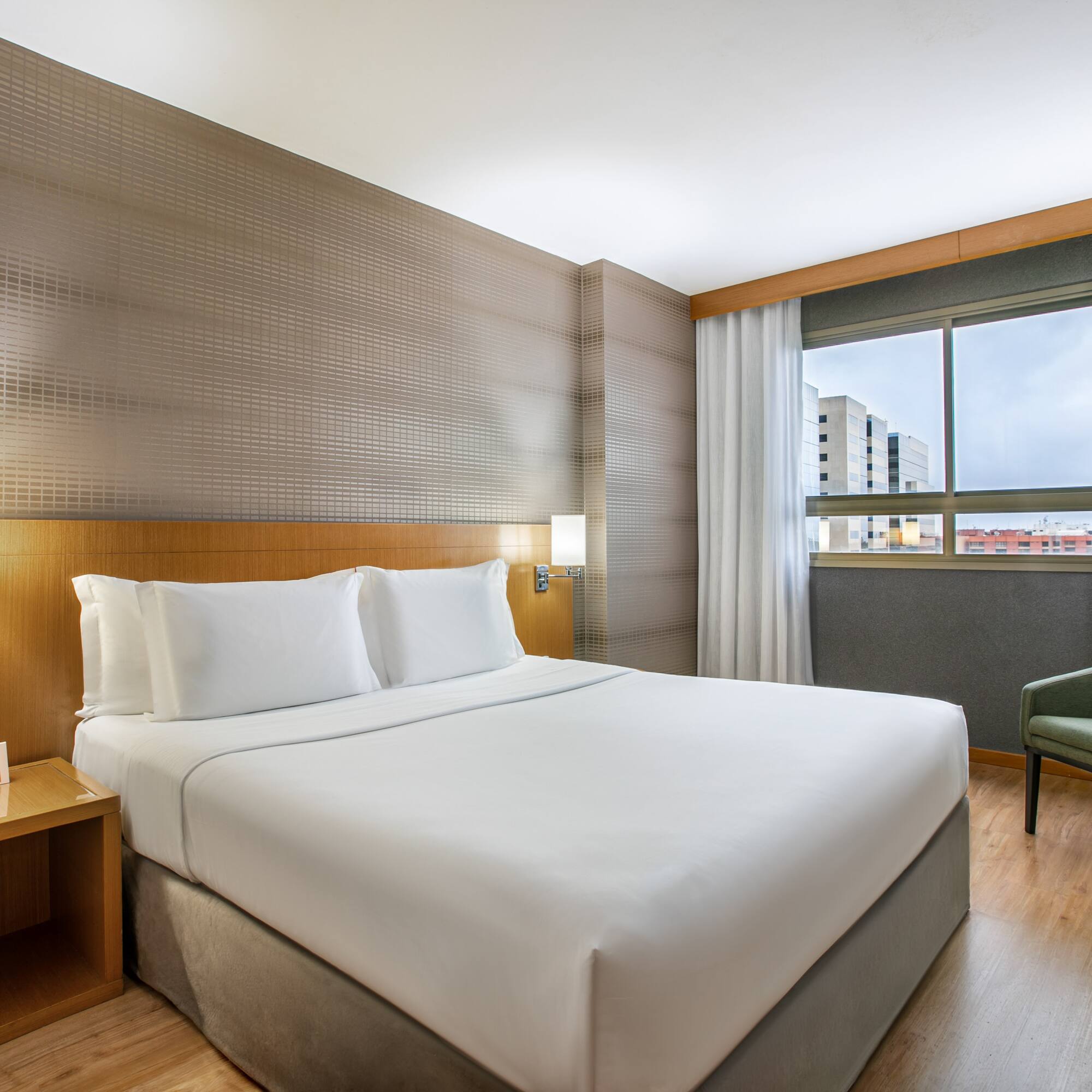 Modern hotel bedroom with king bed, green armchair, and window view.