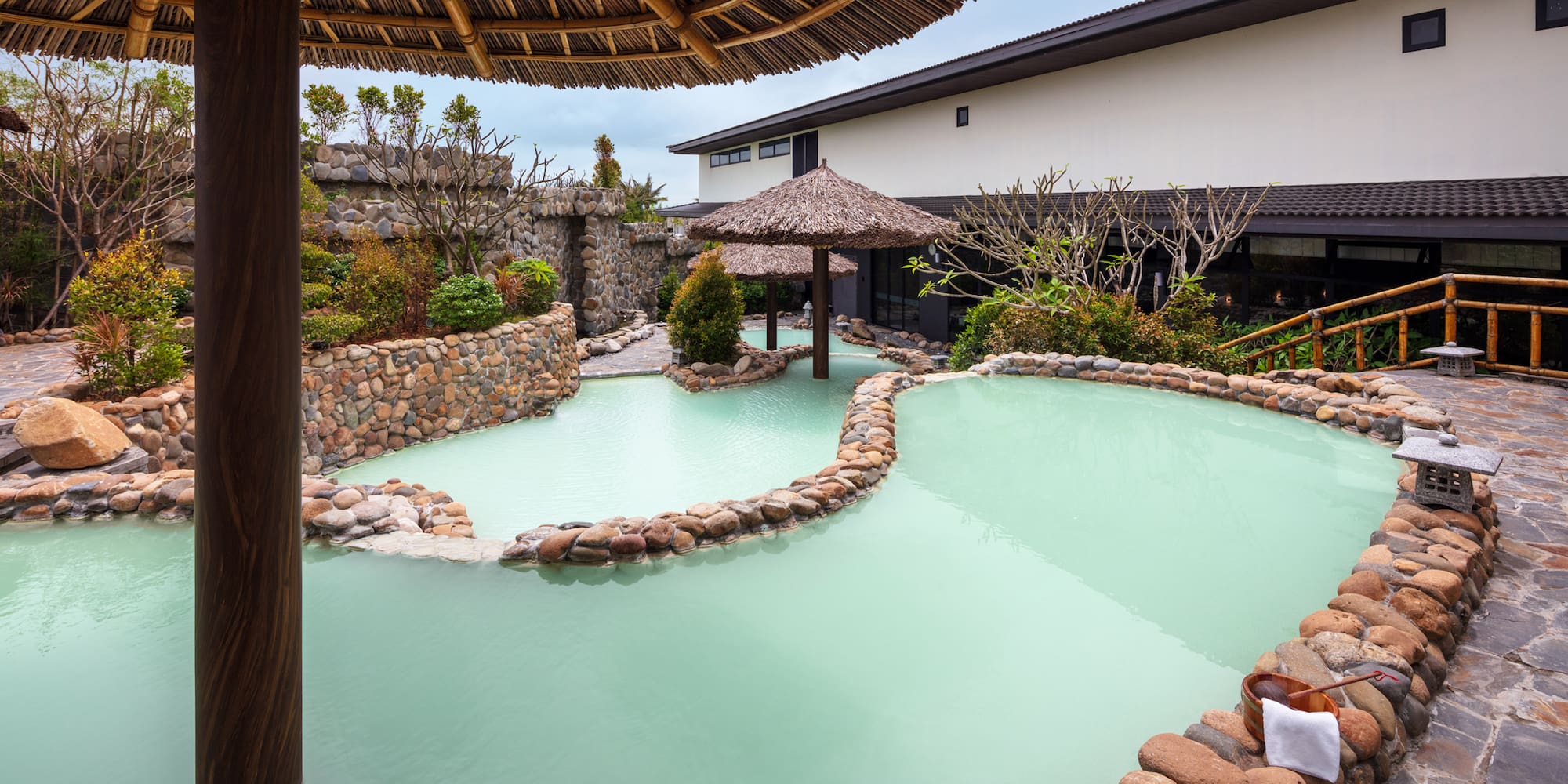 a pool with a straw umbrella and a stone wall