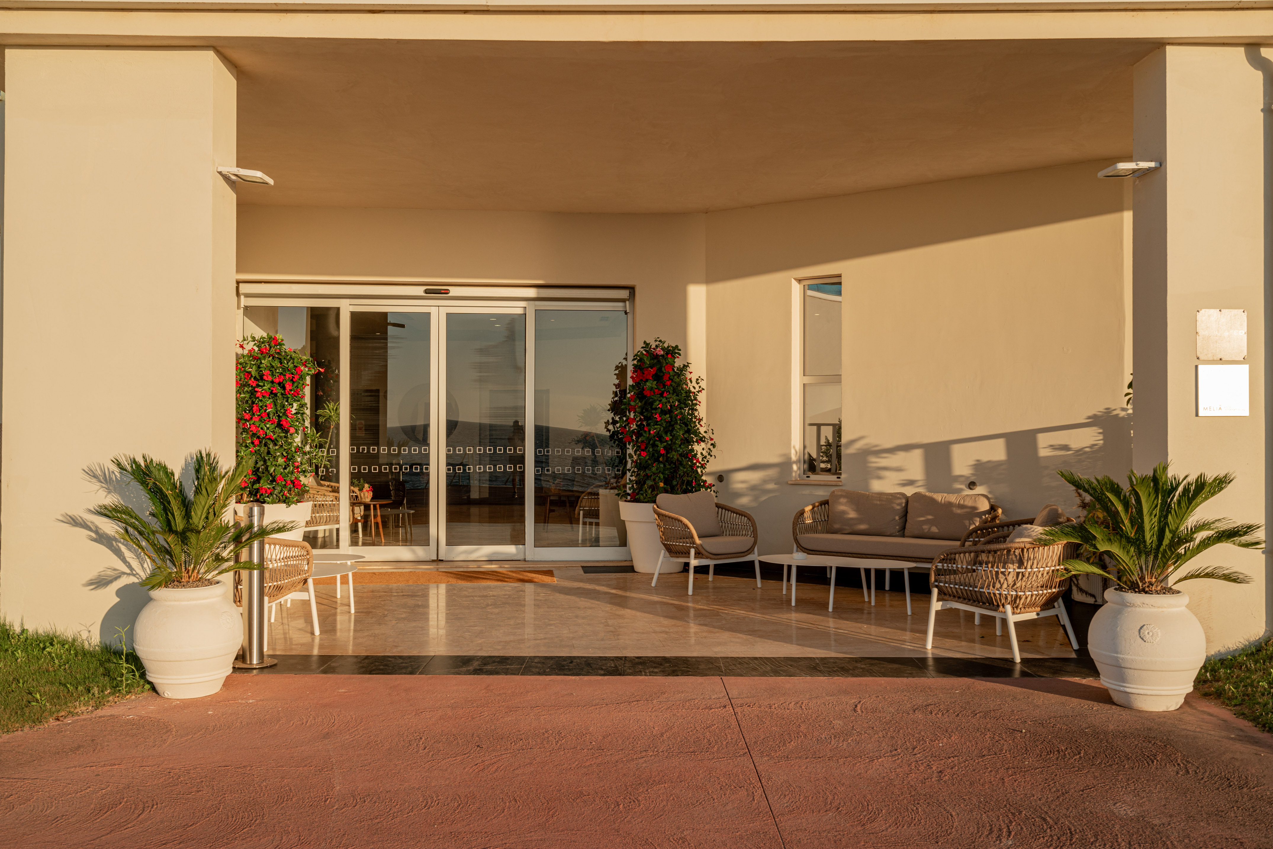 Resort entrance patio with outdoor lounge seating, potted palm plants, and red bougainvillea.