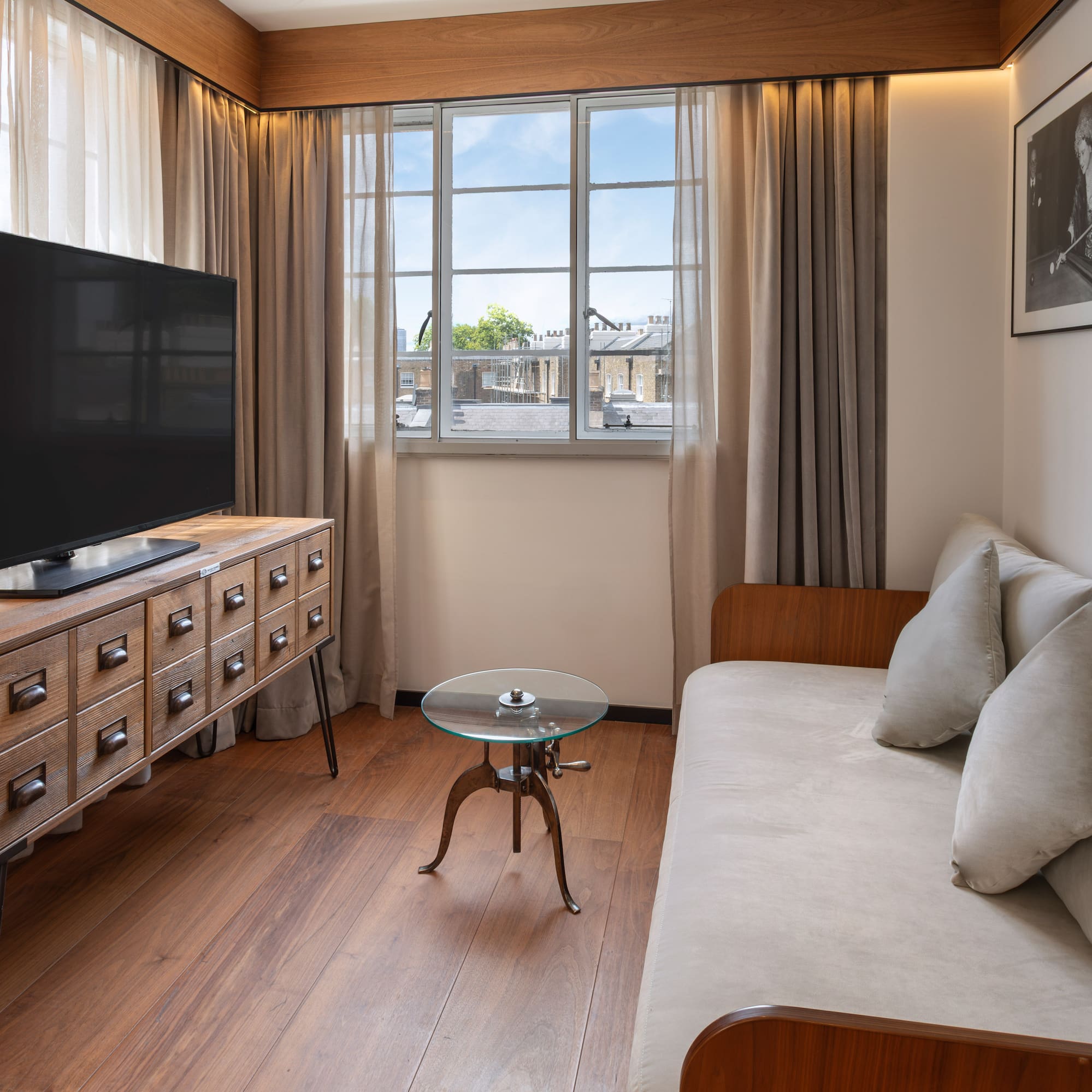 Hotel room living area with TV, wooden media console, sofa, and window view.