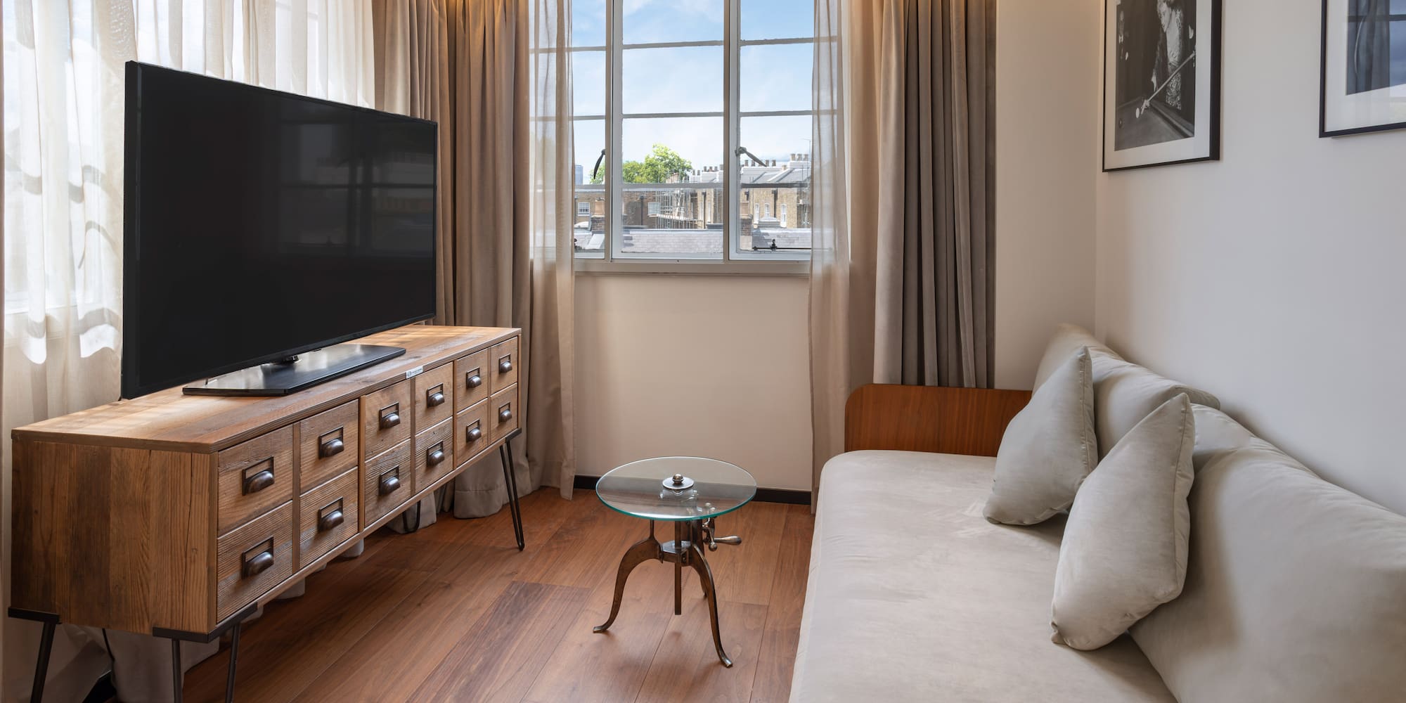 Hotel room living area with TV, wooden media console, sofa, and window view.