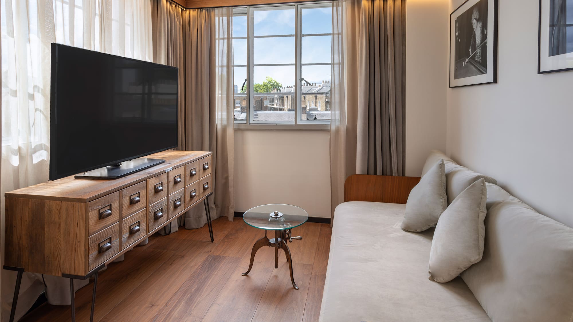 Hotel room living area with TV, wooden media console, sofa, and window view.