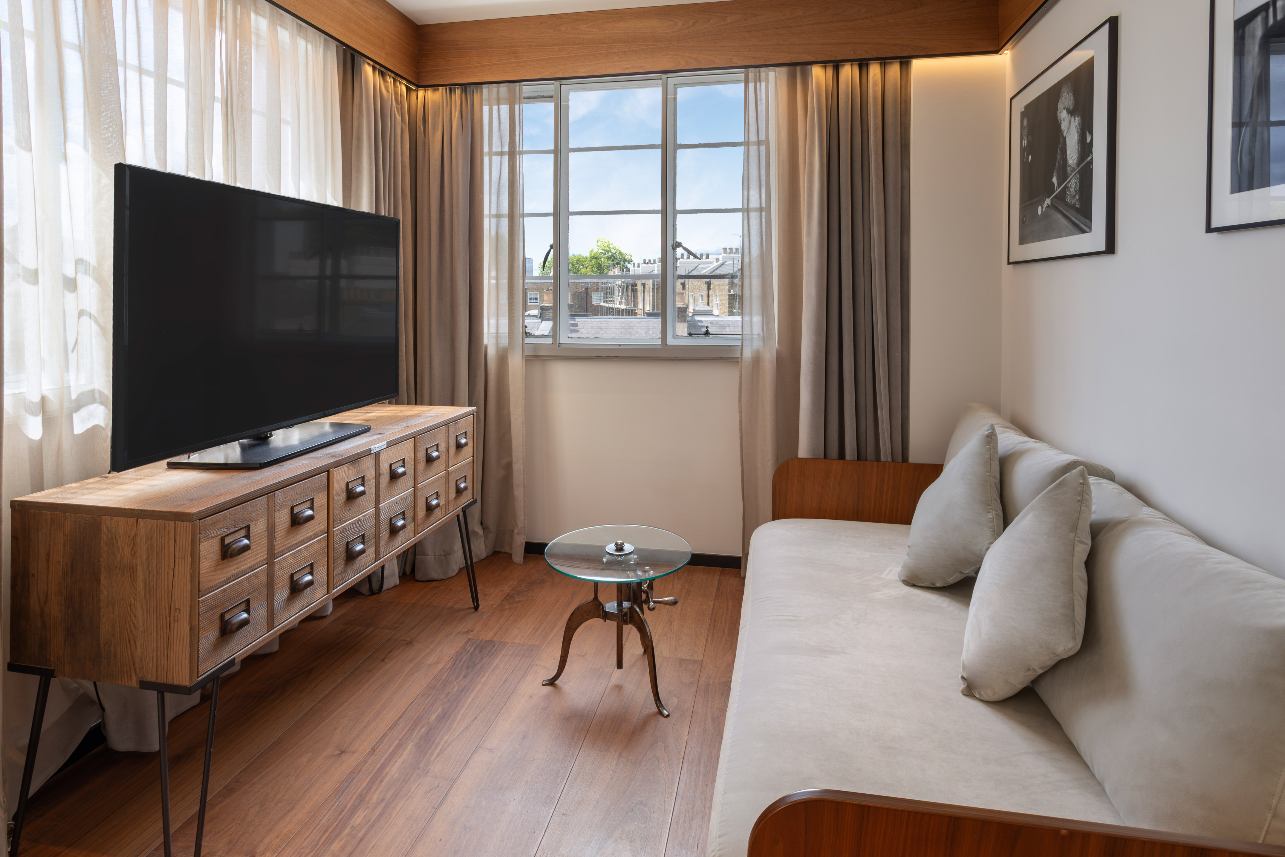 Hotel room living area with TV, wooden media console, sofa, and window view.