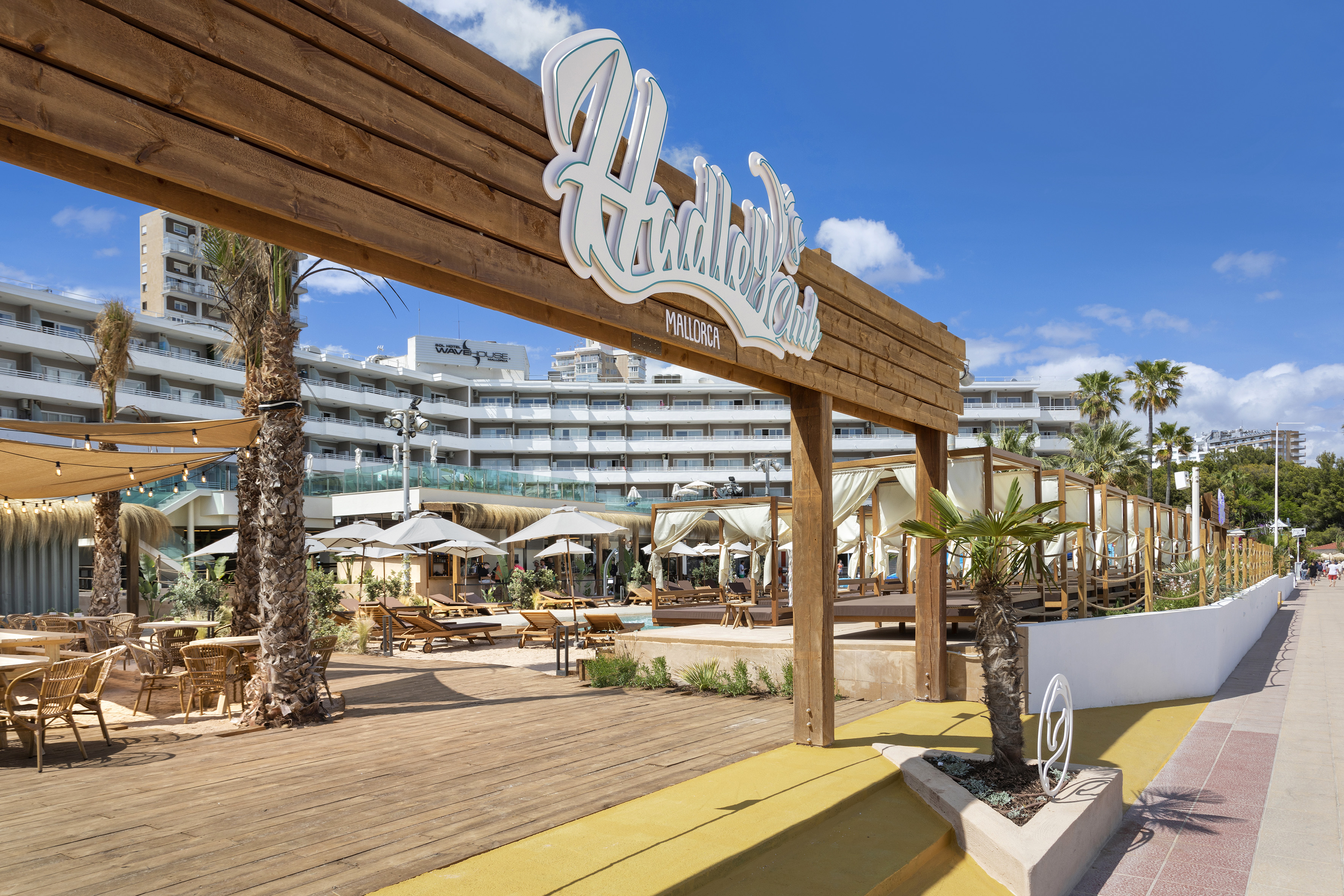 Hadley's Club Mallorca sign at a sunny resort with outdoor lounge and palm trees.