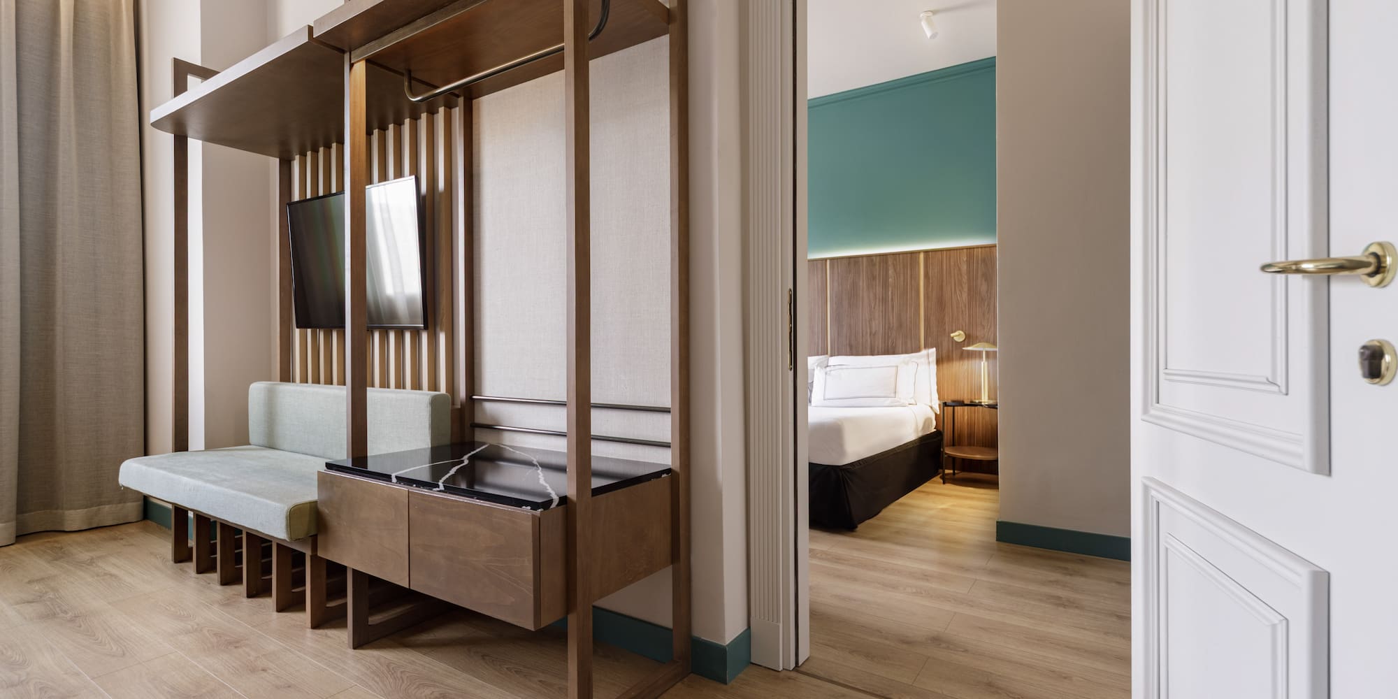 Contemporary hotel suite with wood paneling, living area, and open bedroom door.