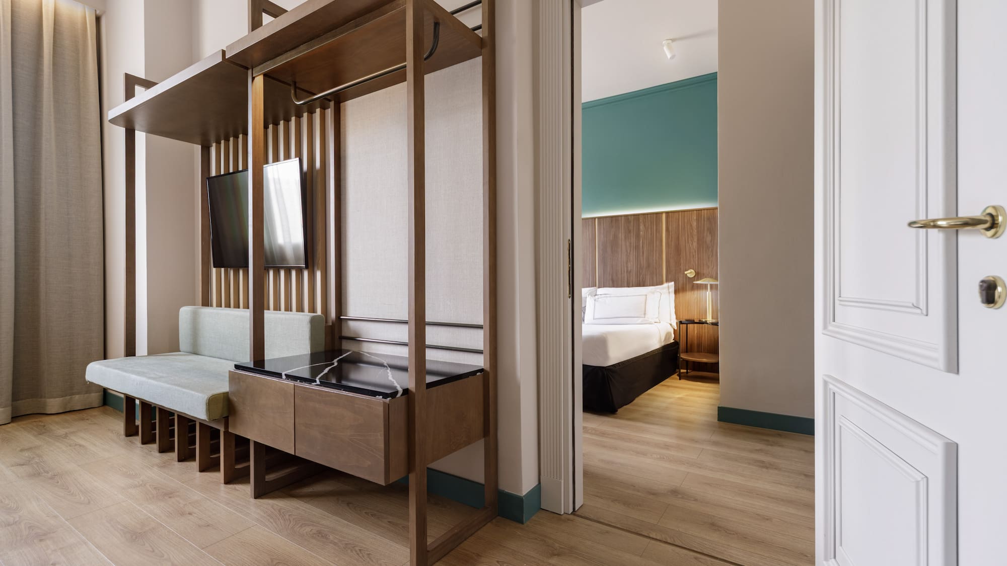 Contemporary hotel suite with wood paneling, living area, and open bedroom door.