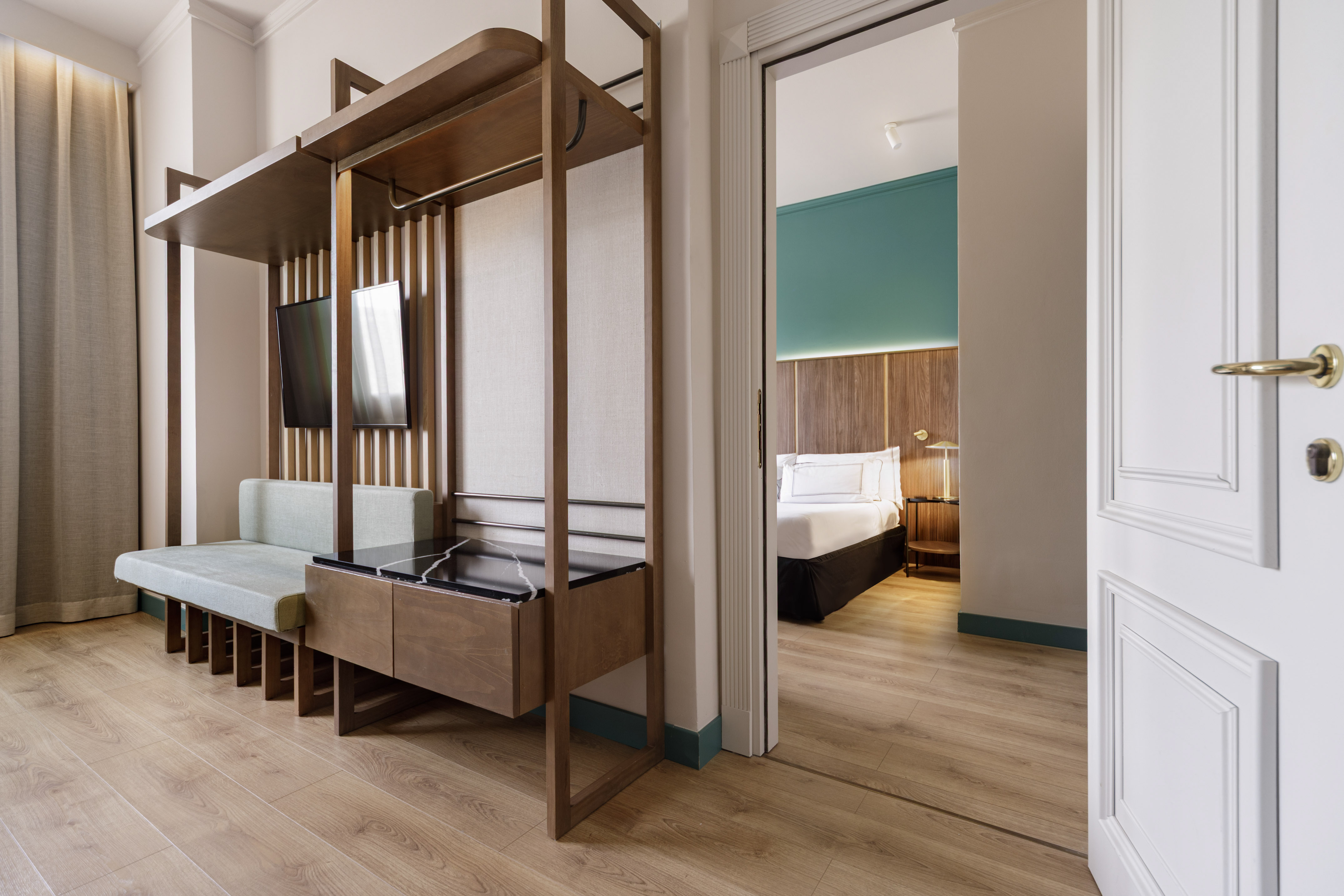 Contemporary hotel suite with wood paneling, living area, and open bedroom door.