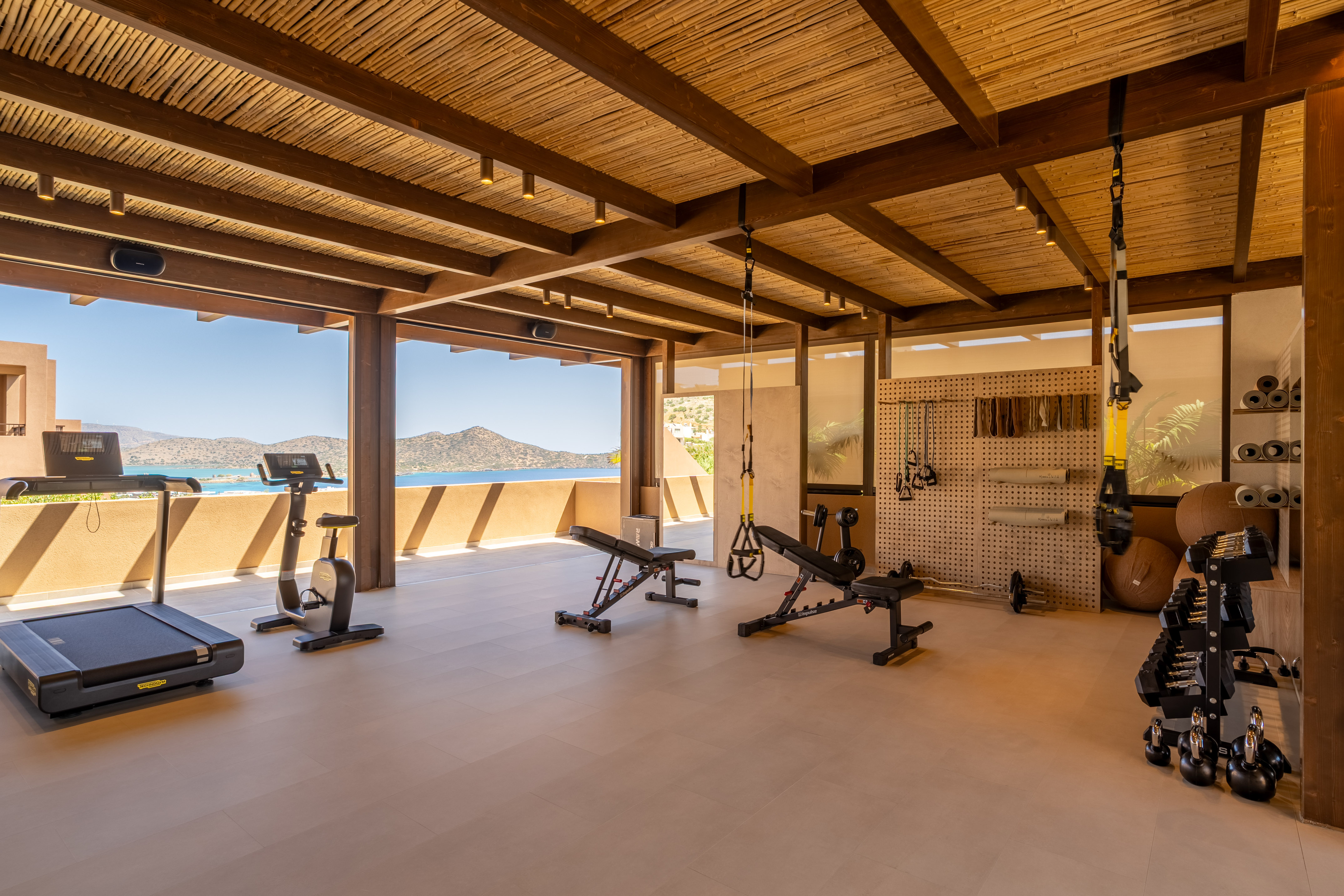 Open-air resort gym with sea view, treadmill, bike, weight benches, and dumbbells.