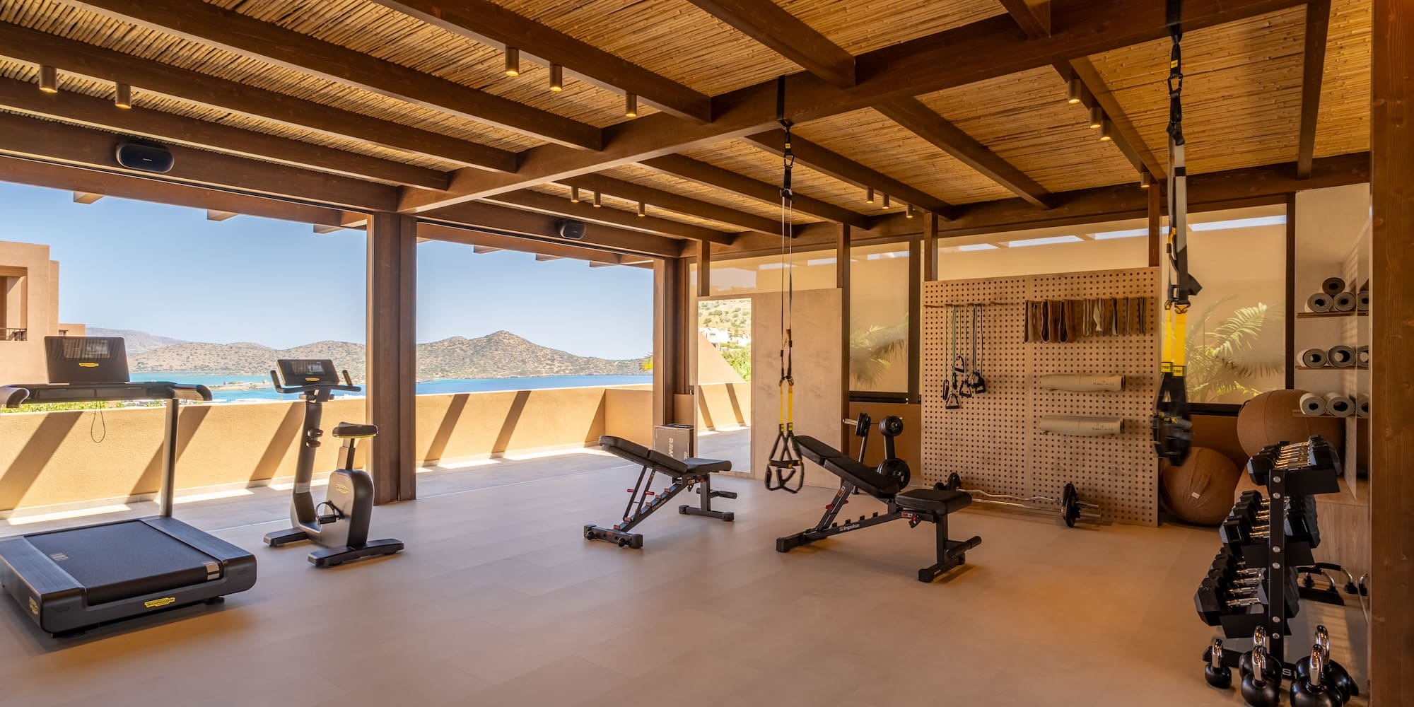Open-air resort gym with sea view, treadmill, bike, weight benches, and dumbbells.