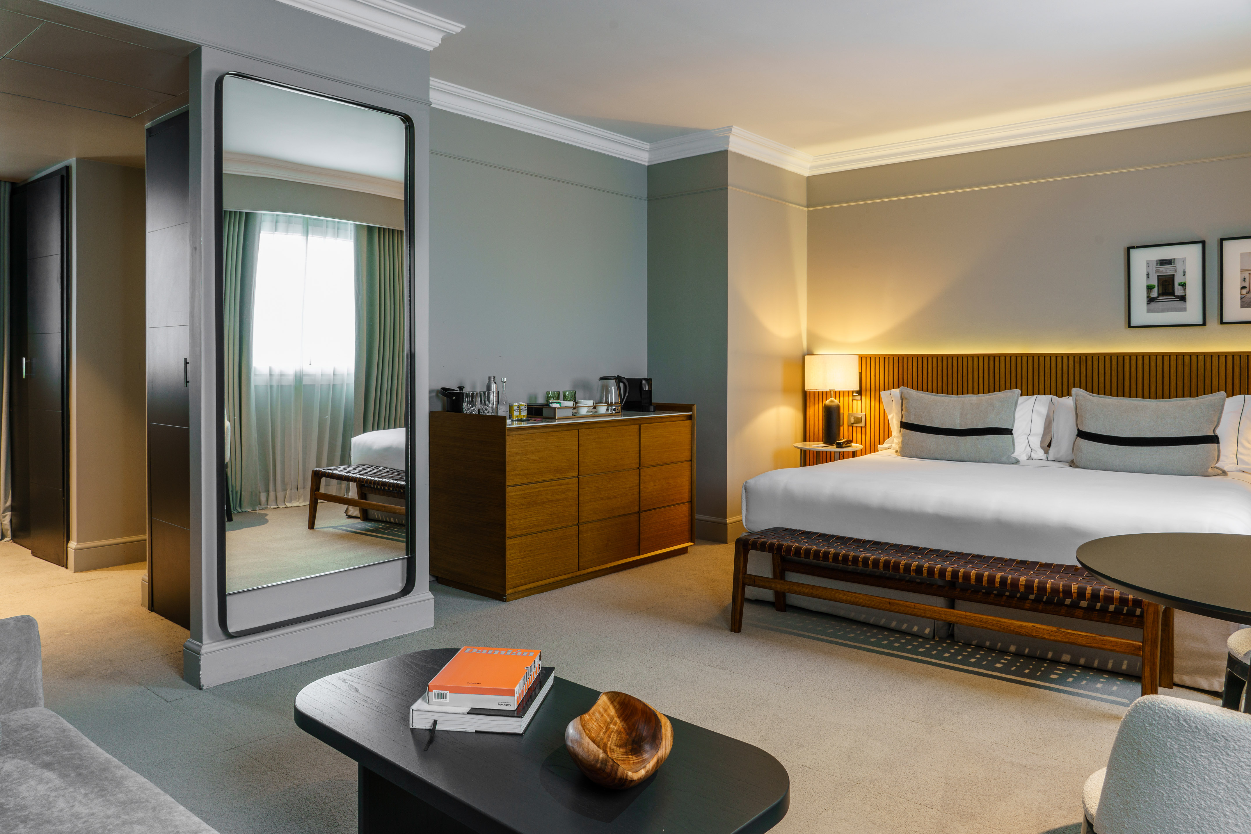 Elegant hotel bedroom featuring a bed, wooden dresser, coffee table, and large mirror.