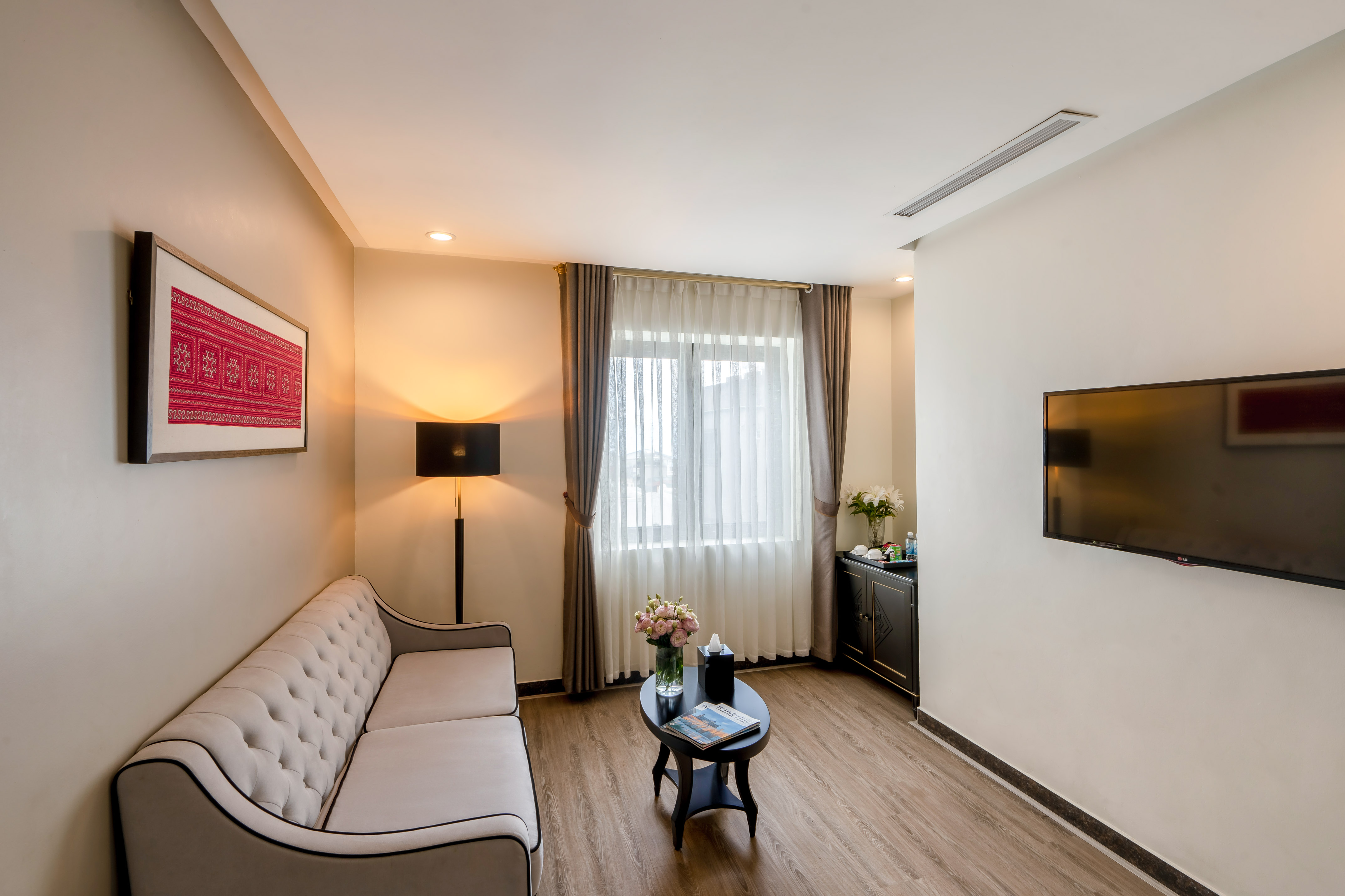 Modern hotel living room with tufted sofa, coffee table, and flat-screen TV.