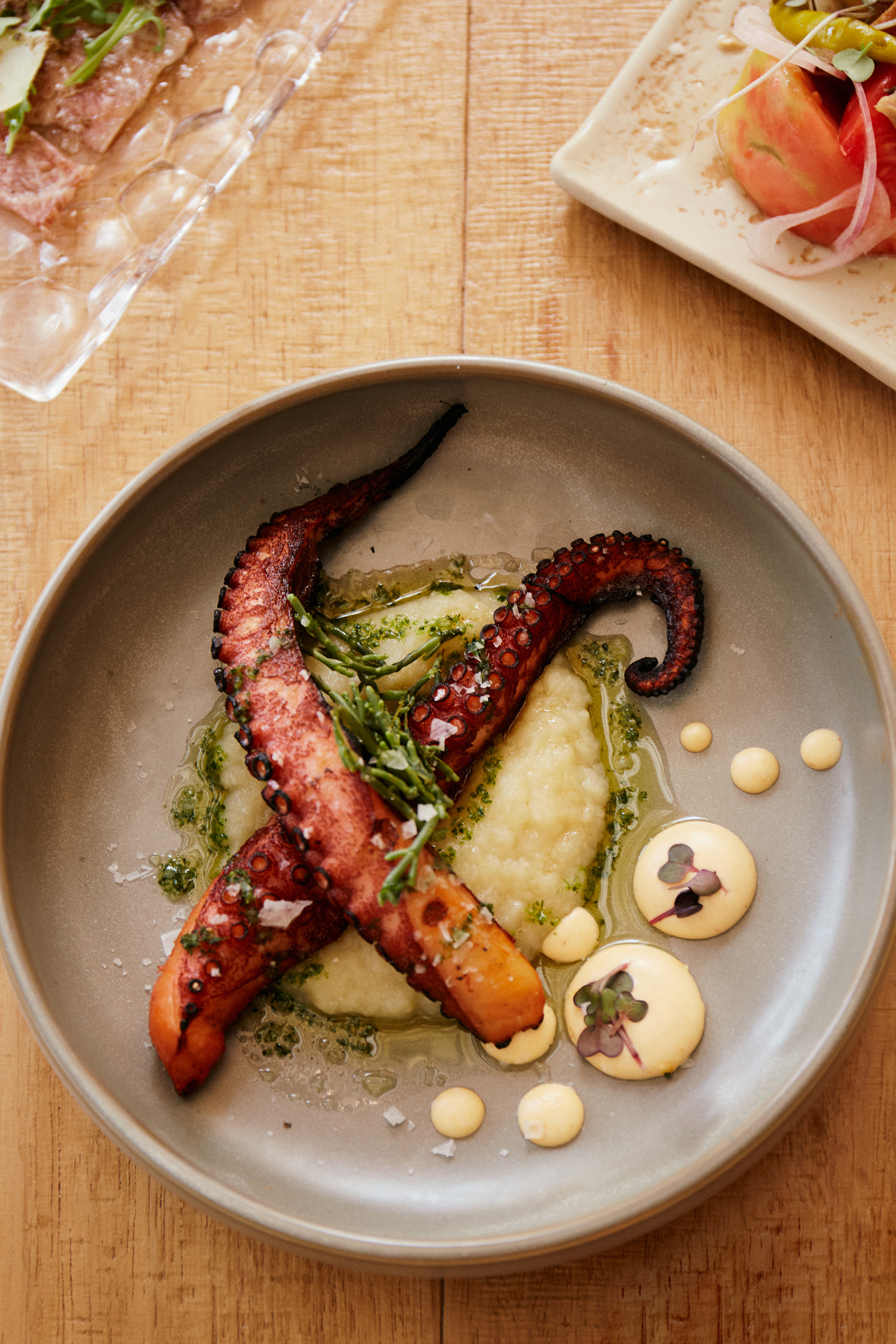 Grilled octopus with potato puree, samphire, and aioli dots on a plate.