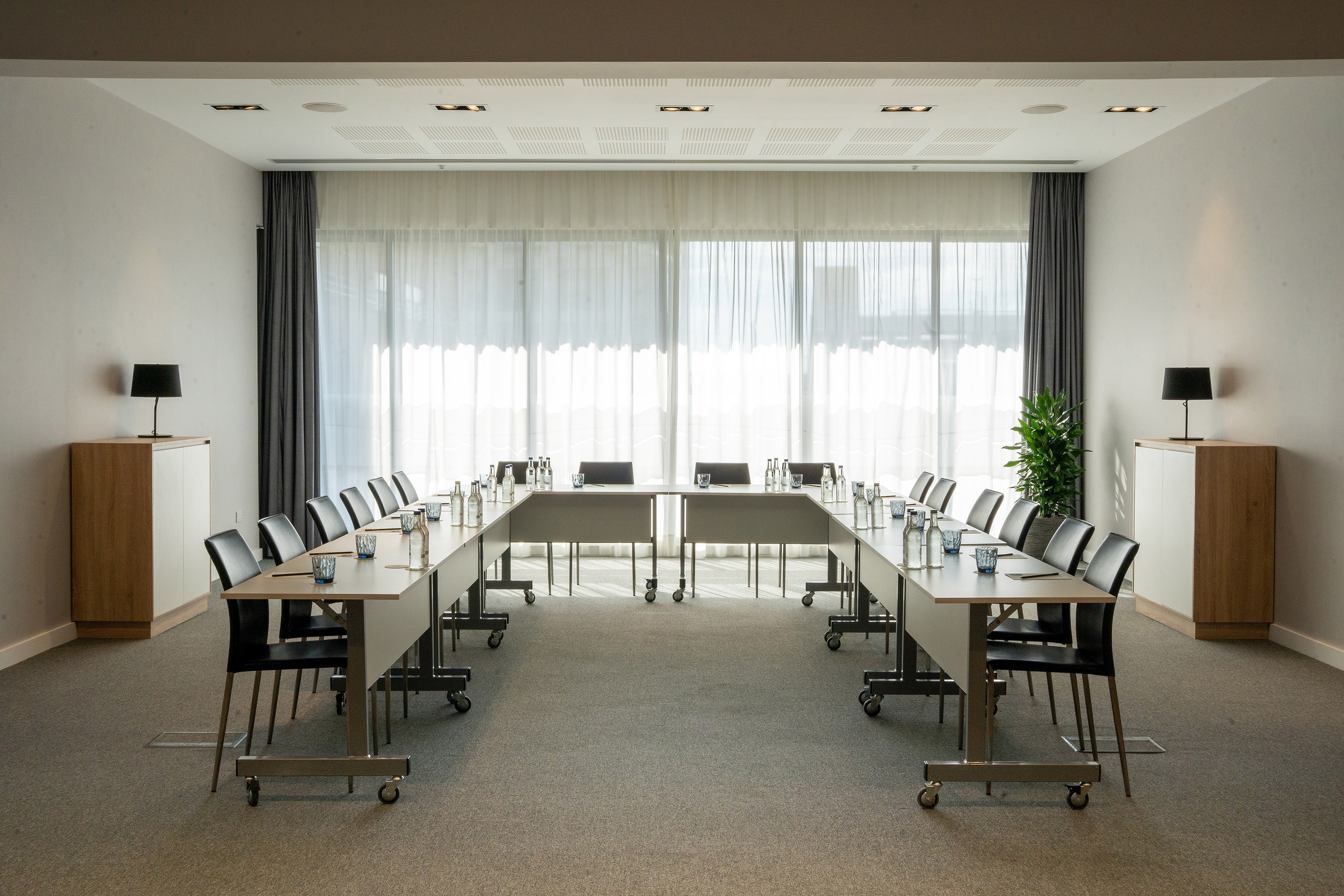 Modern U-shape conference room with tables, chairs, and bright window.