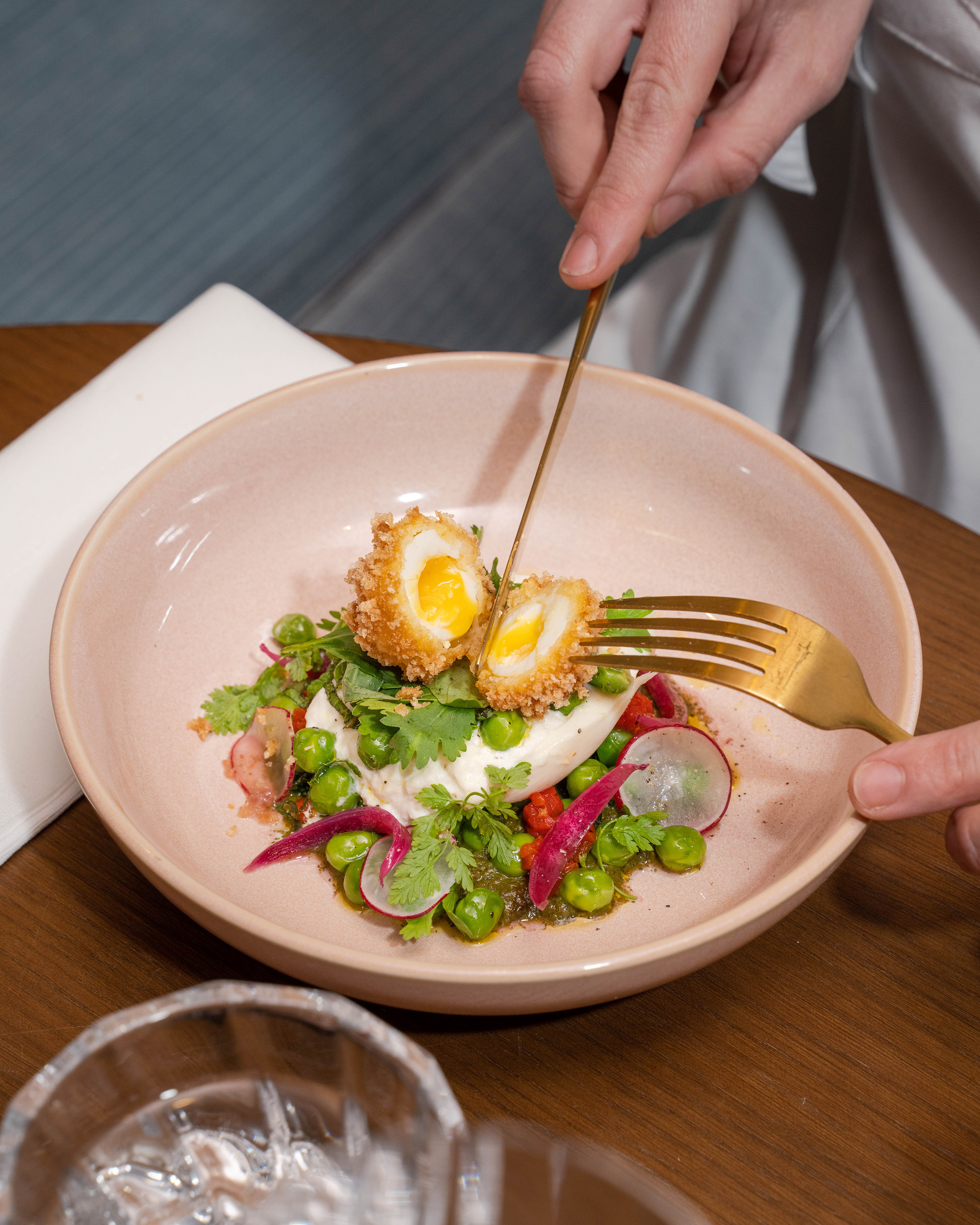 Crispy fried egg with runny yolk, peas, radish, and burrata, cut by hands.