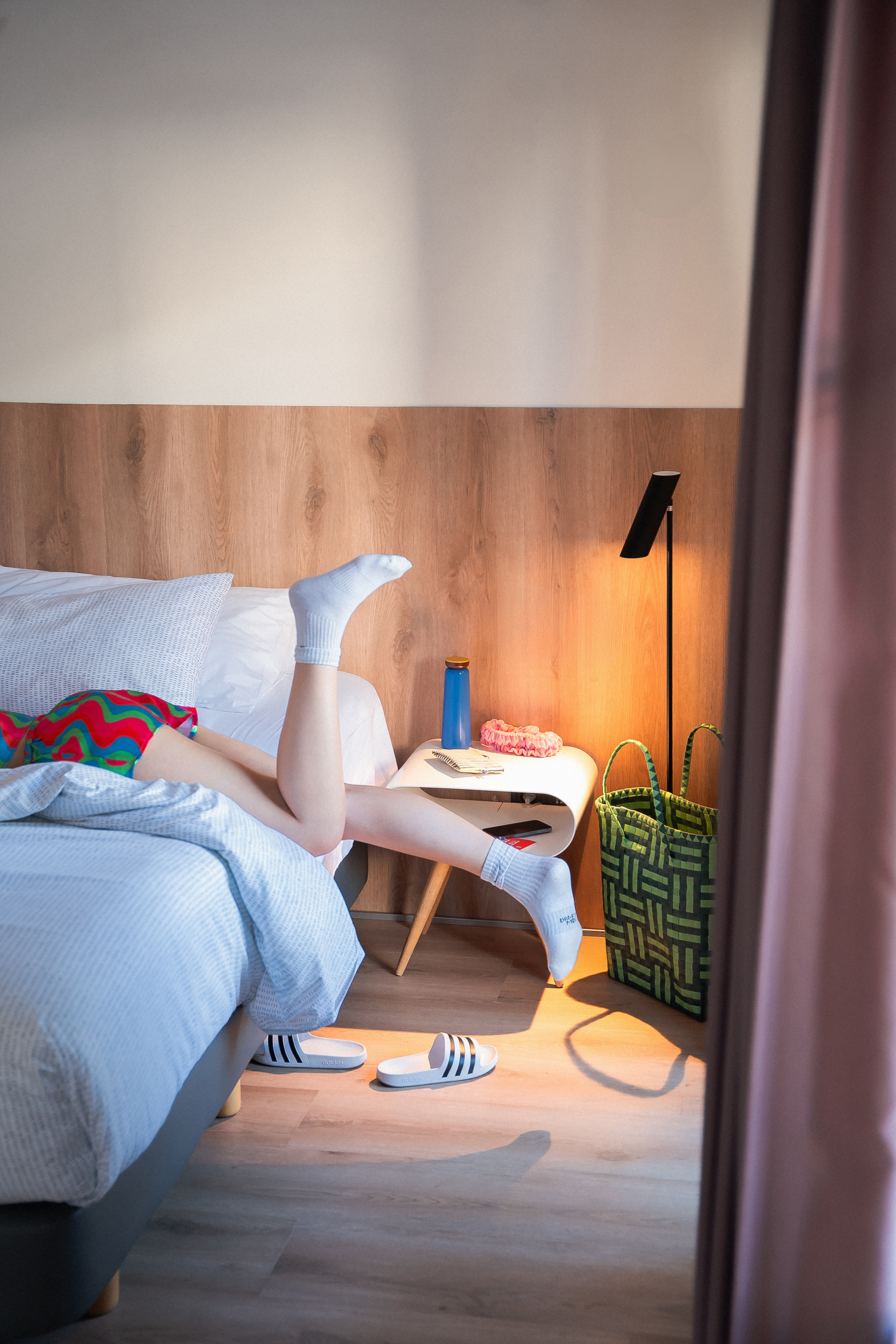 Legs in white socks resting on bed, modern bedroom with bedside table.