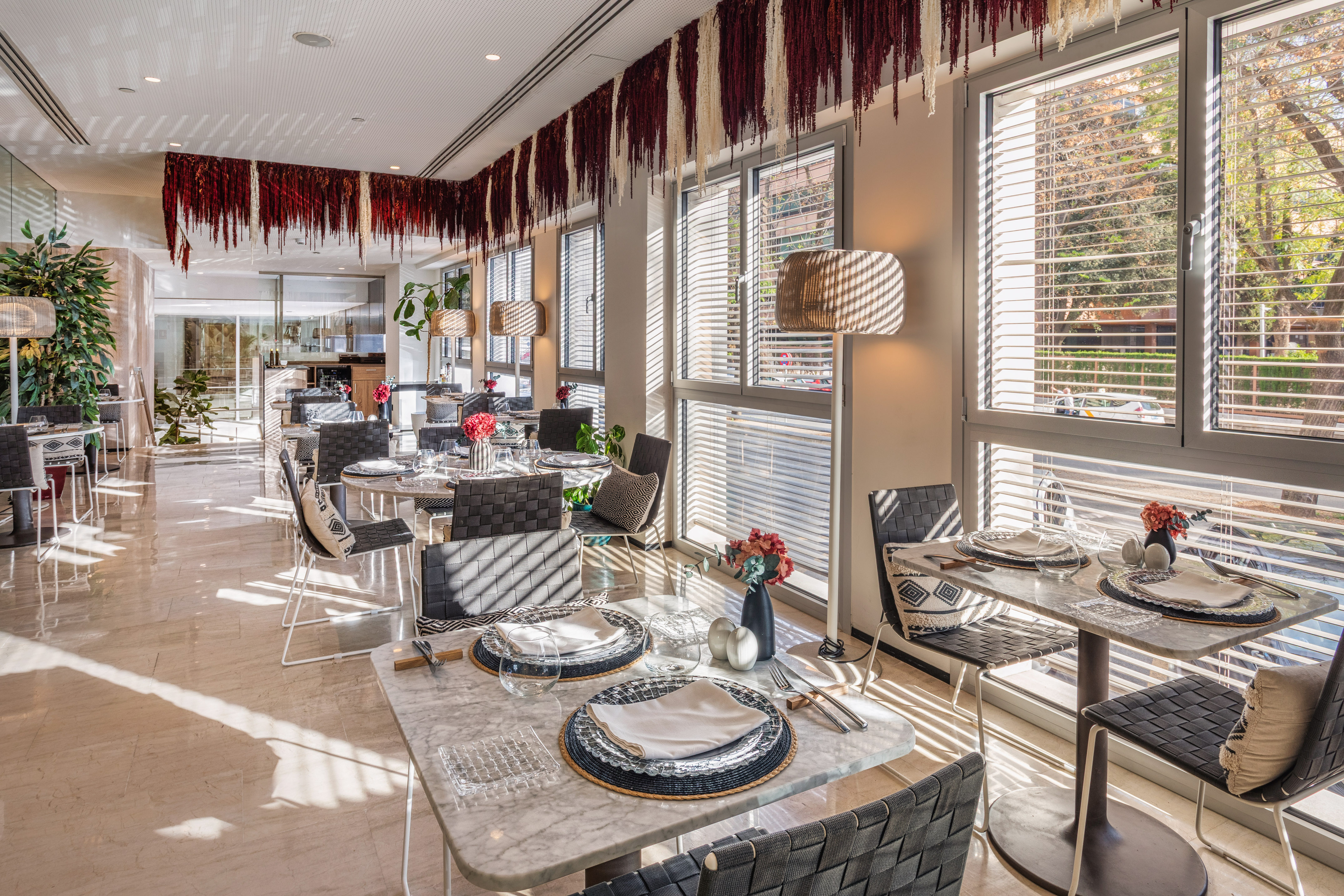 Sunlit modern dining room with set tables, large windows, and decorative ceiling.