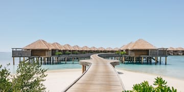 a walkway leading to a beach with huts on stilts