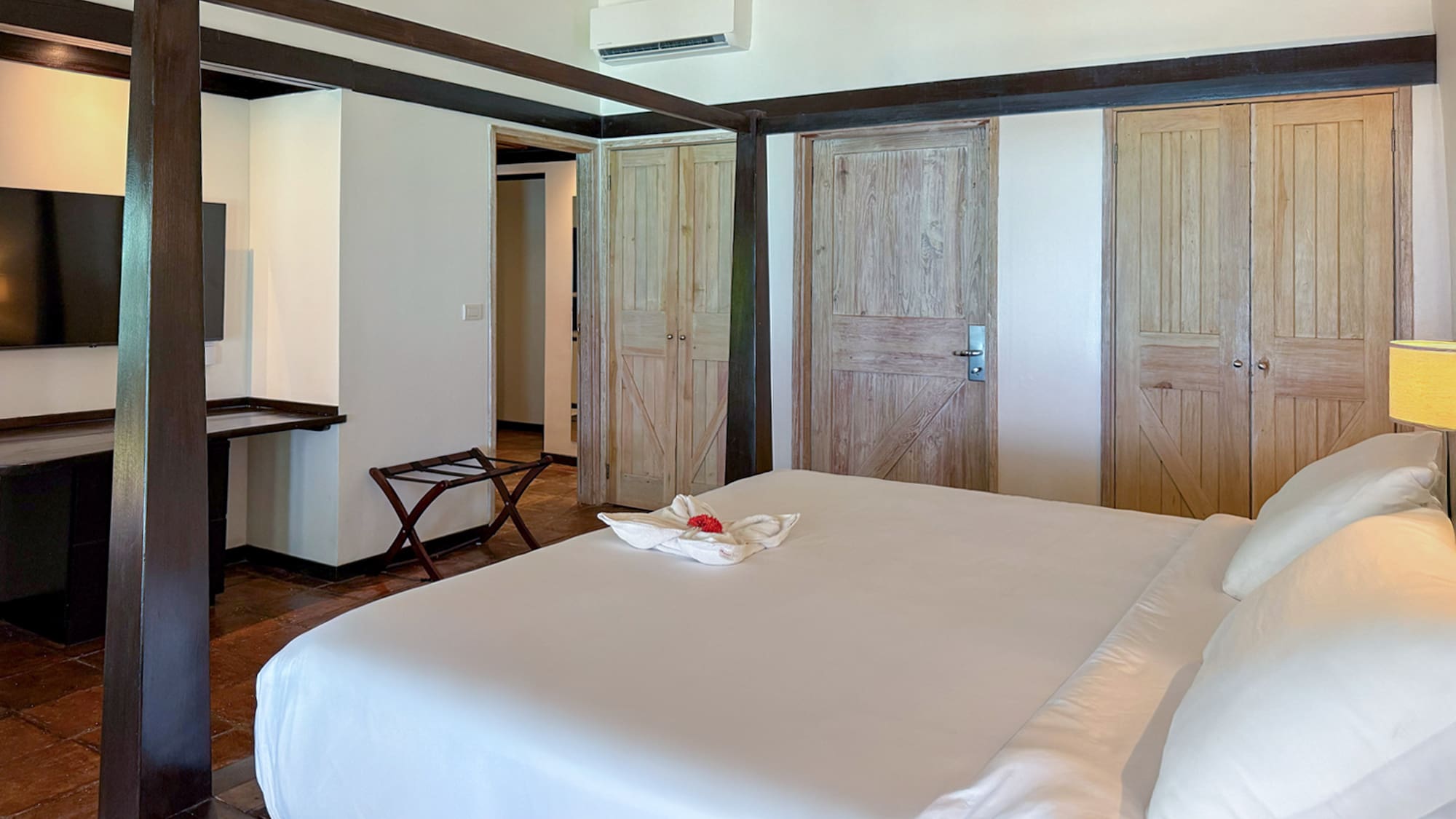 Tropical hotel bedroom with dark four-poster bed, white bedding, wooden doors.