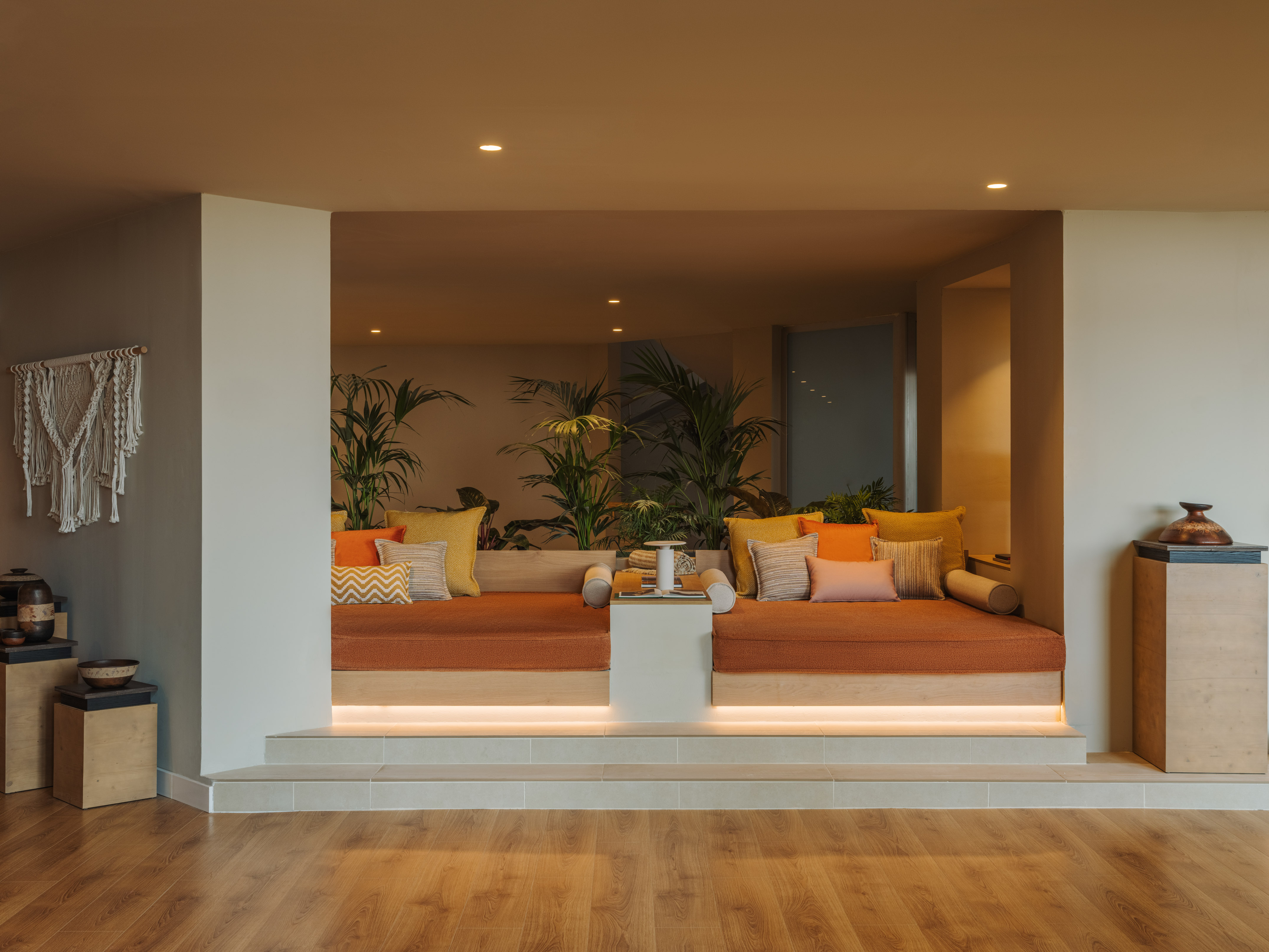 Cozy recessed lounge with orange benches, colorful pillows, and tropical plants.