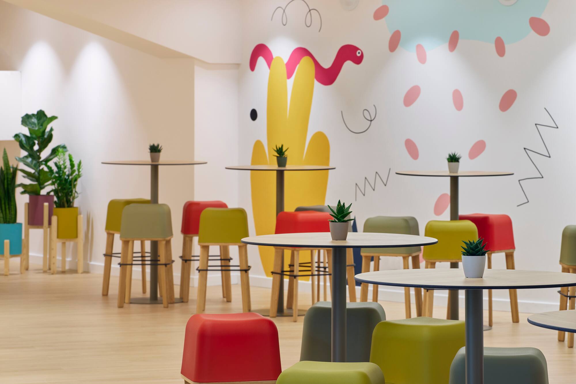 Colorful modern cafe with playful wall art, small tables, and bright stools.
