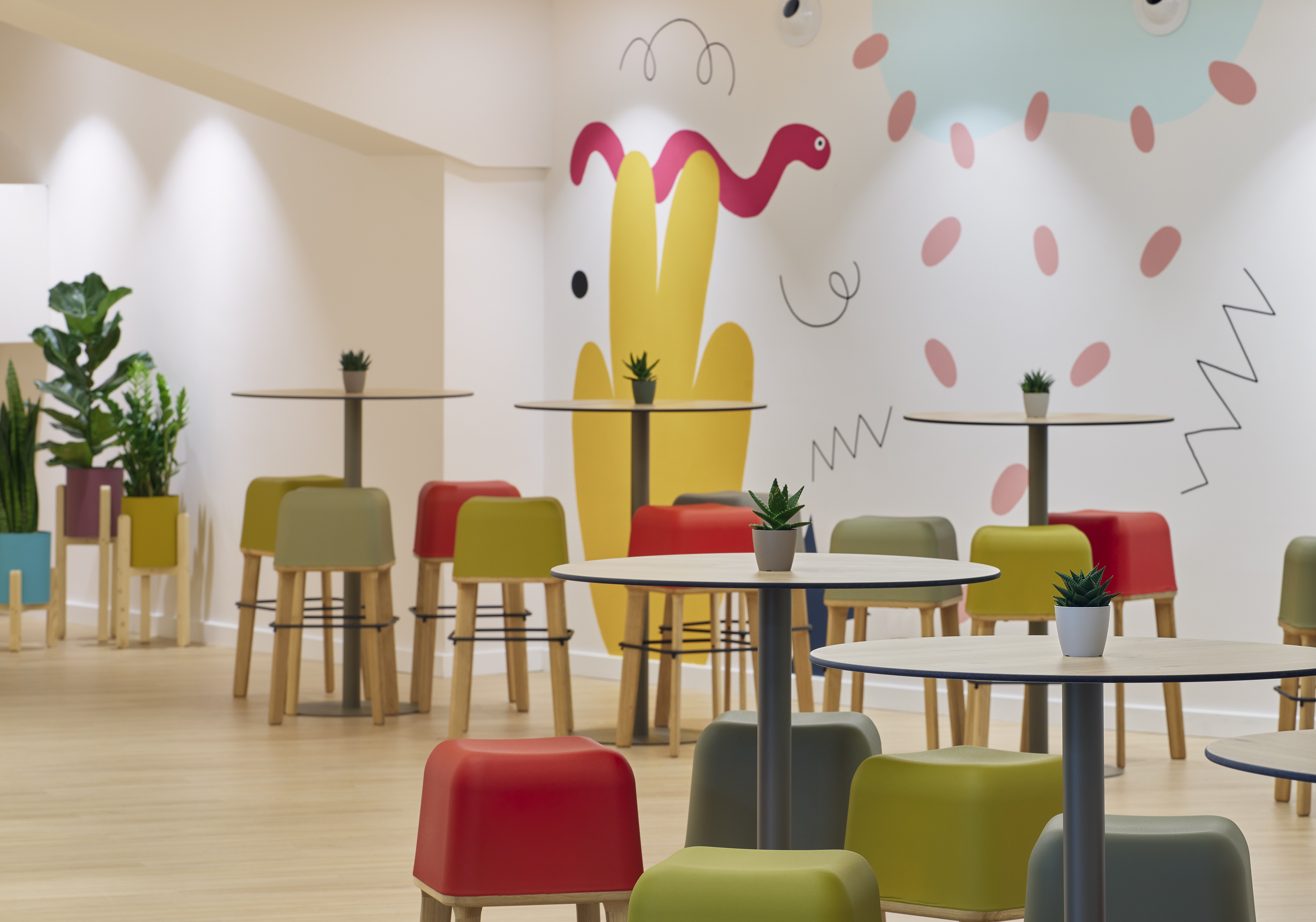 Colorful modern cafe with playful wall art, small tables, and bright stools.