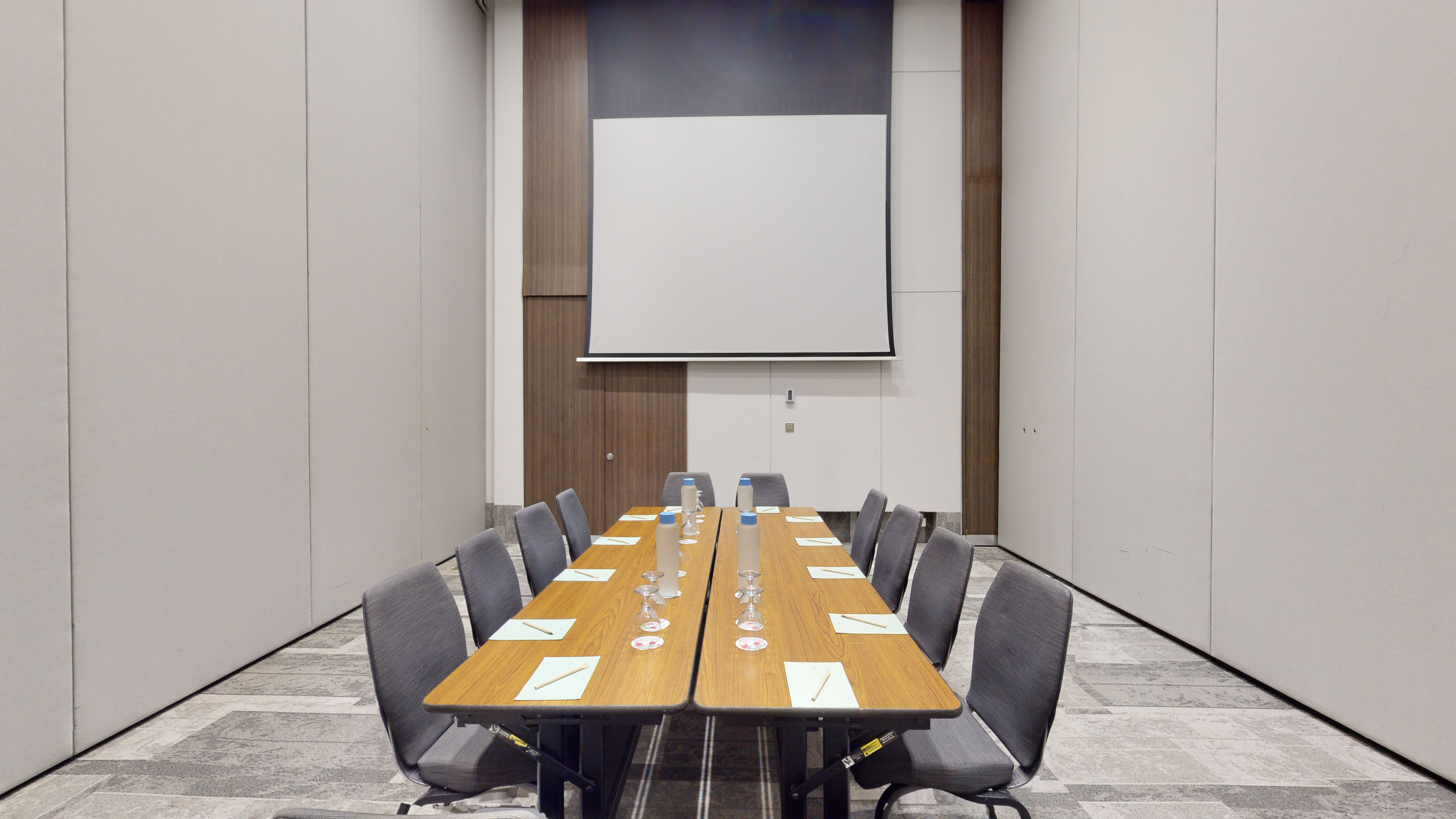 Modern conference room with boardroom table, gray chairs, and projector screen.